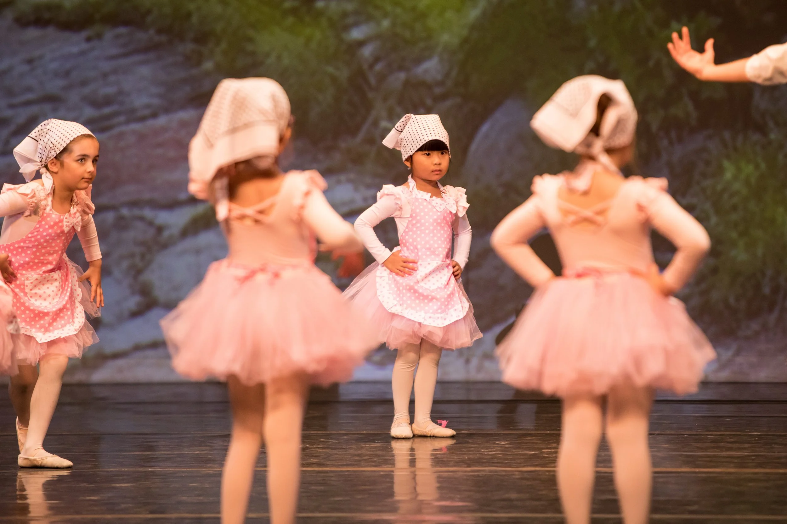 Jeunes filles en costume de ballet rose avec chaussons roses, en train de pratiquer ou de se préparer pour une performance sur scène, avec un décor de fond naturel.
