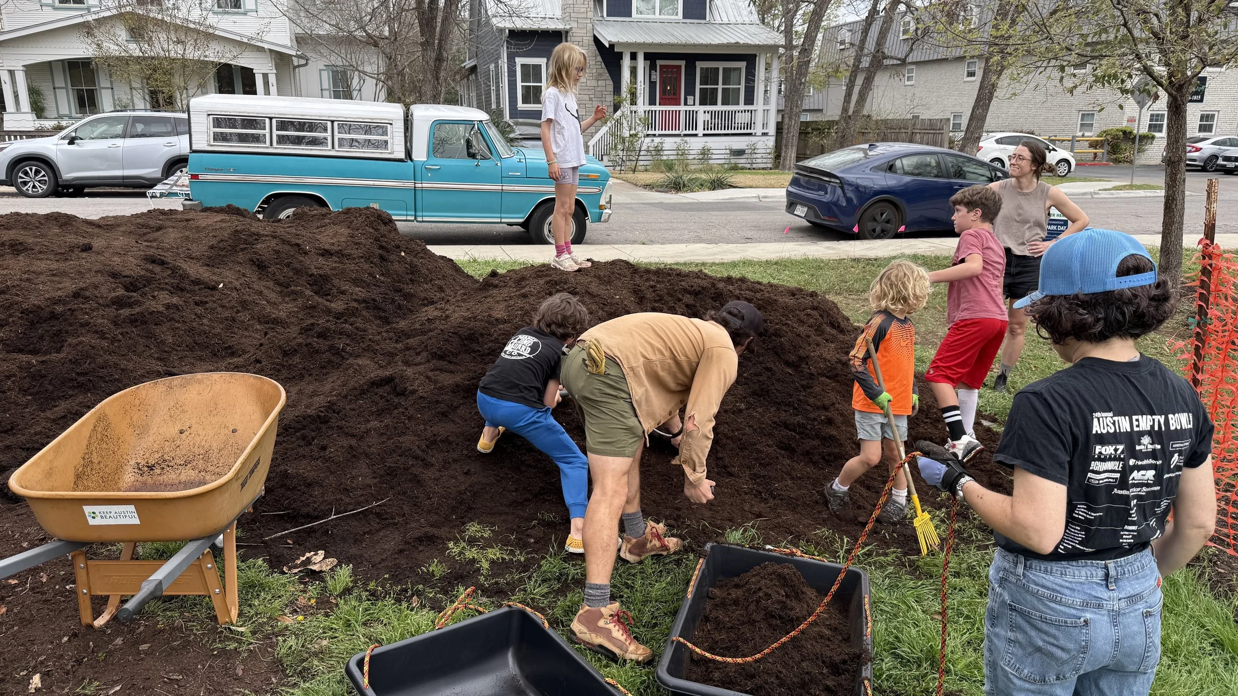 Multiple people planting and digging in a park with trees and a basketball court in the background.