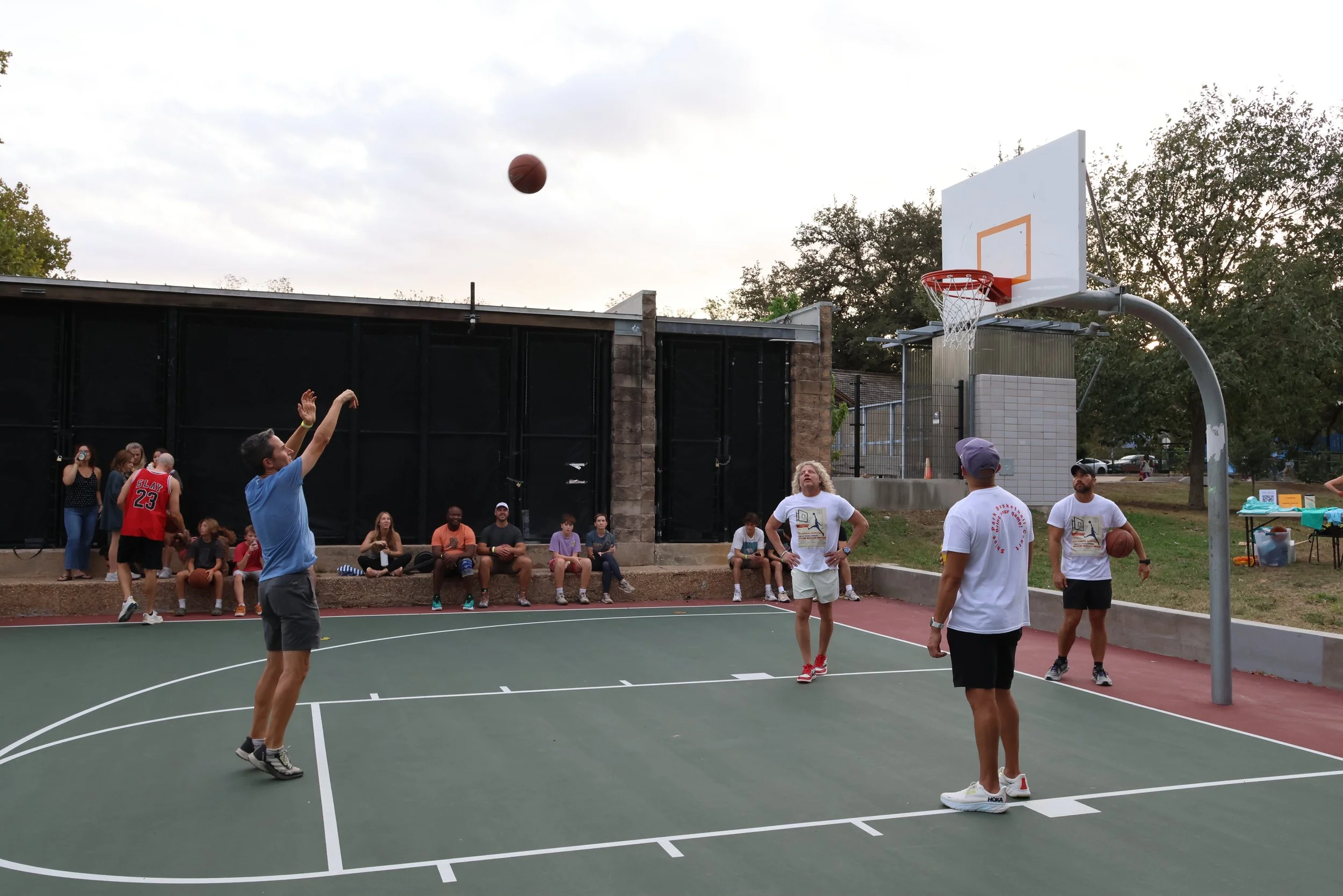 Players shooting hoops at Shipe Park's basketball courts with a crowd of onlookers.