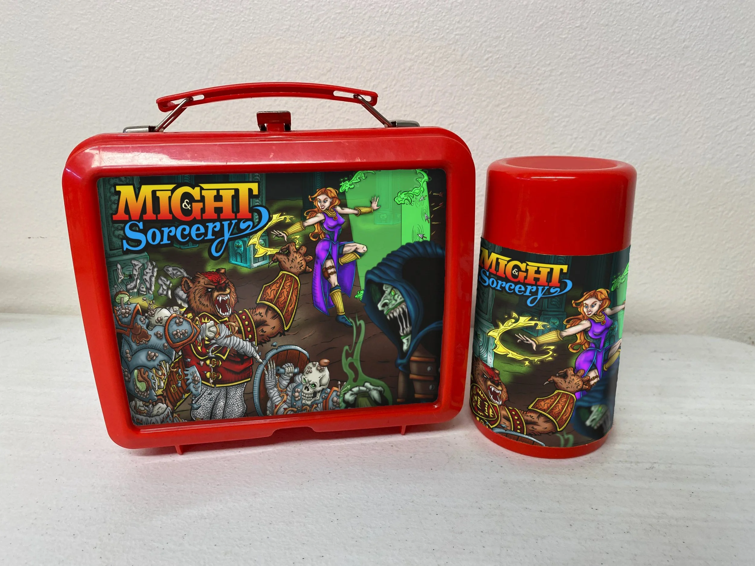 An Old school Lunch Box mockup showing the Might & Sorcery cover art and logo