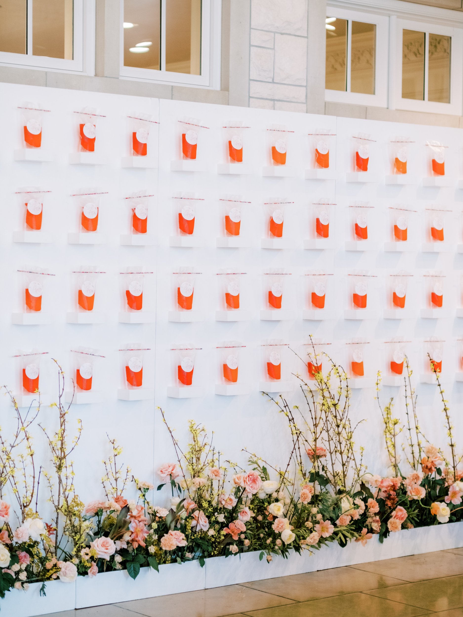 a large white wall with orange items on it with white boxes lining the floor and orange and yellow flowers with greenery lining the boxes