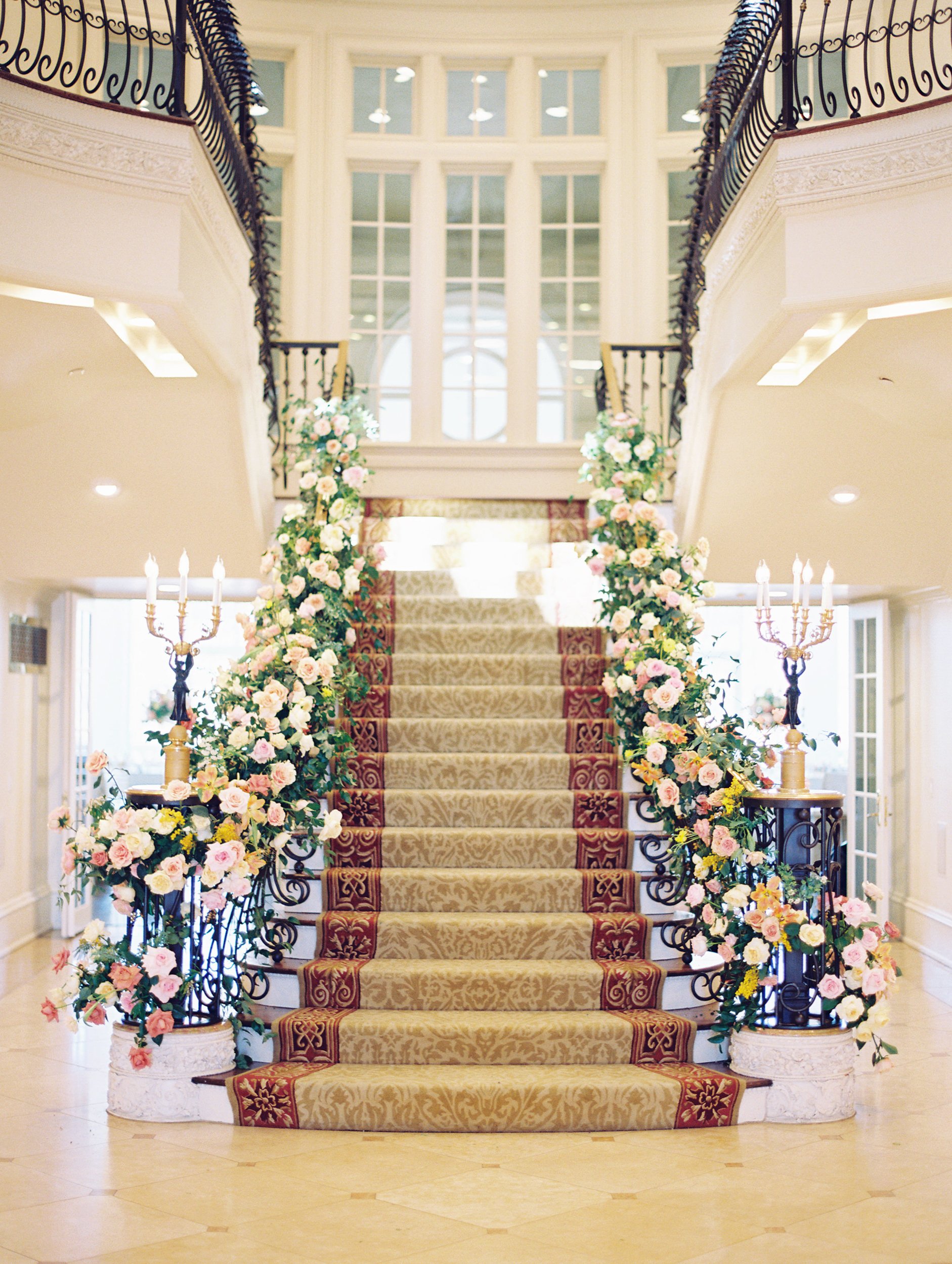 a staircase with flowers on each side of the handrails and gold and red carpet on stairs and feaux candlestick on each side
