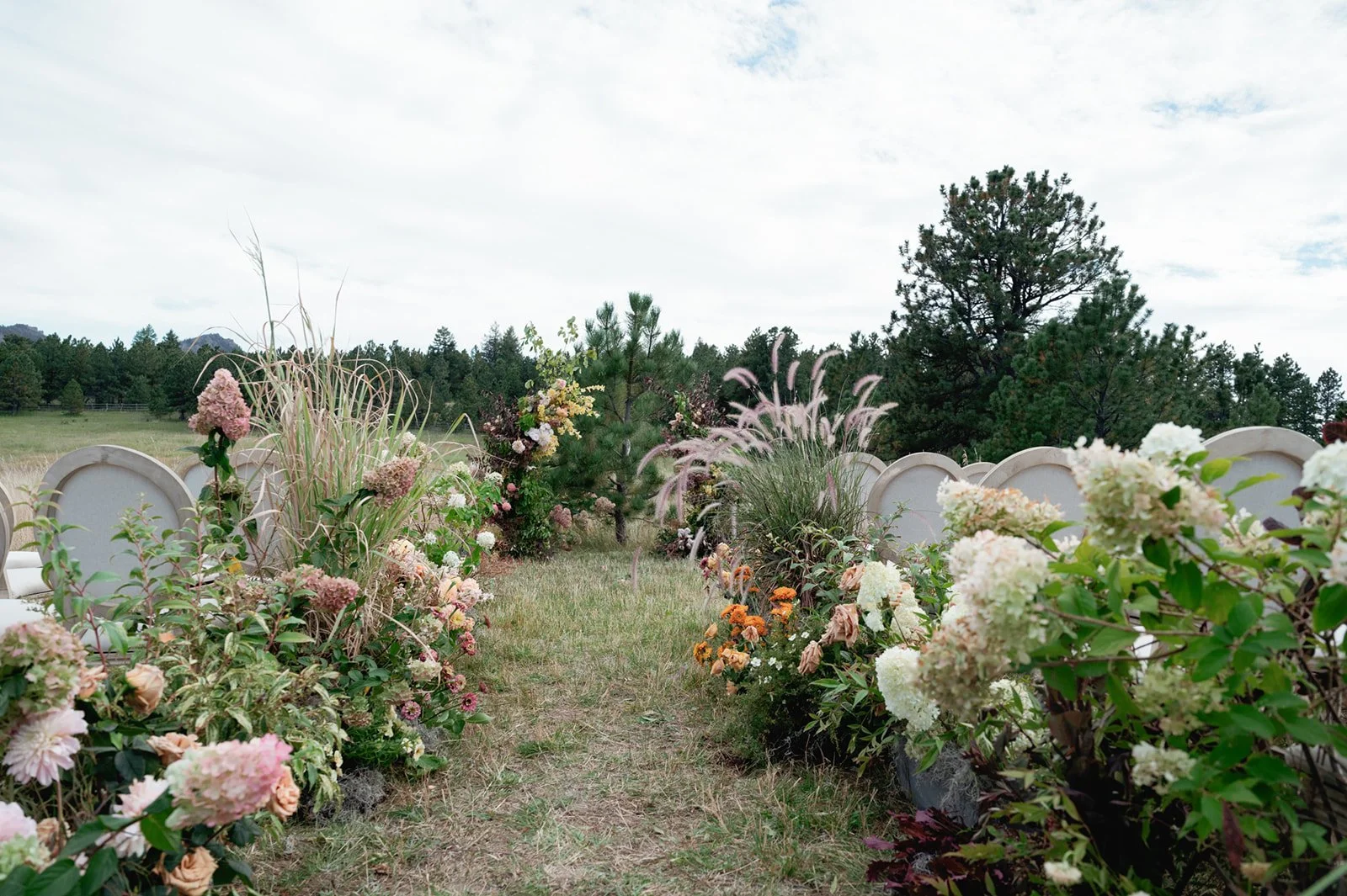 mixed blush and orange flowers down an aisle with grasses and chairs