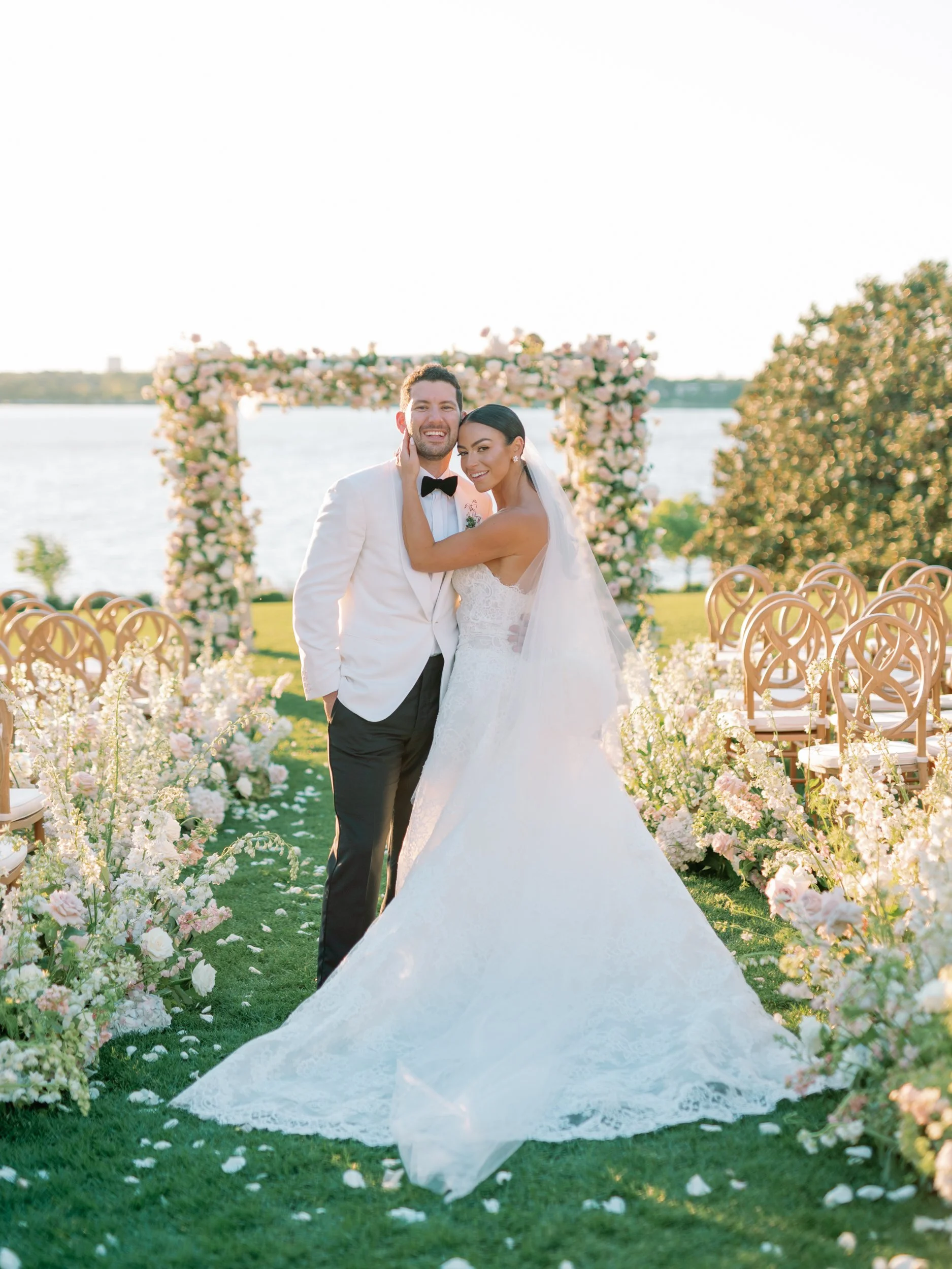 brides and groom looking at the cameral with tall white and nude flowers lining the aisle