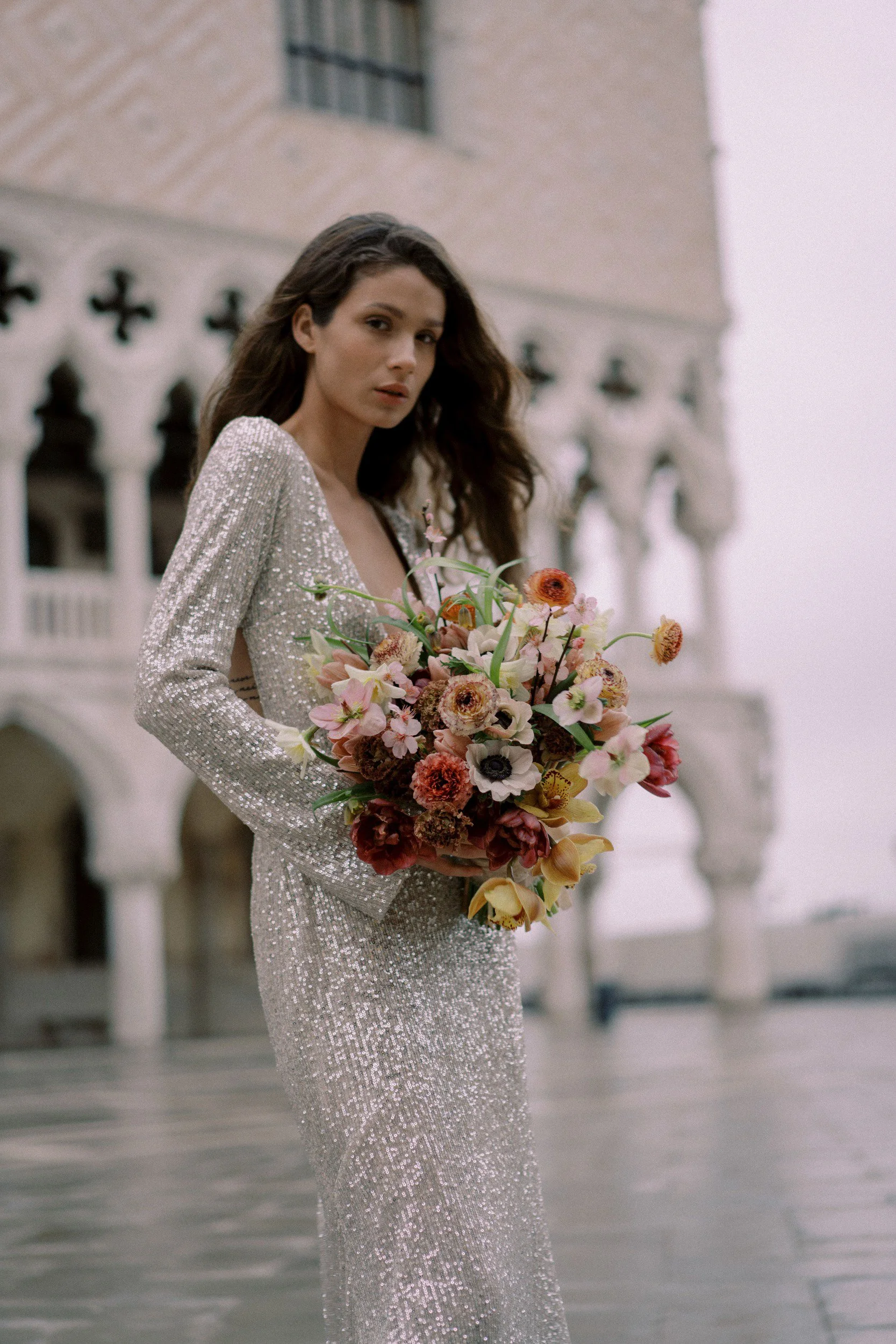 bride in couture gown holding a lush bouquet consisting of anemones, ranunculus, and hellebore in Venice