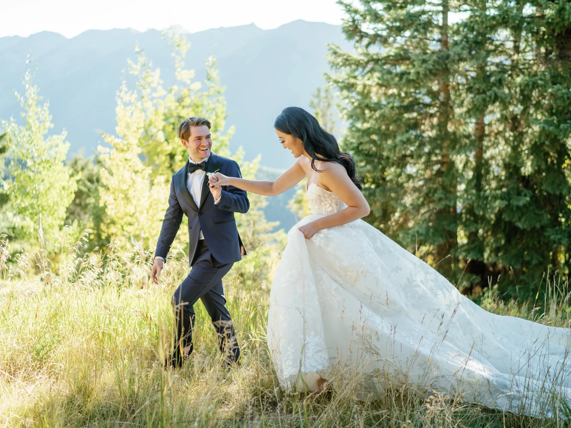 bride and groom walking through a field together holding hands with sunset on them
