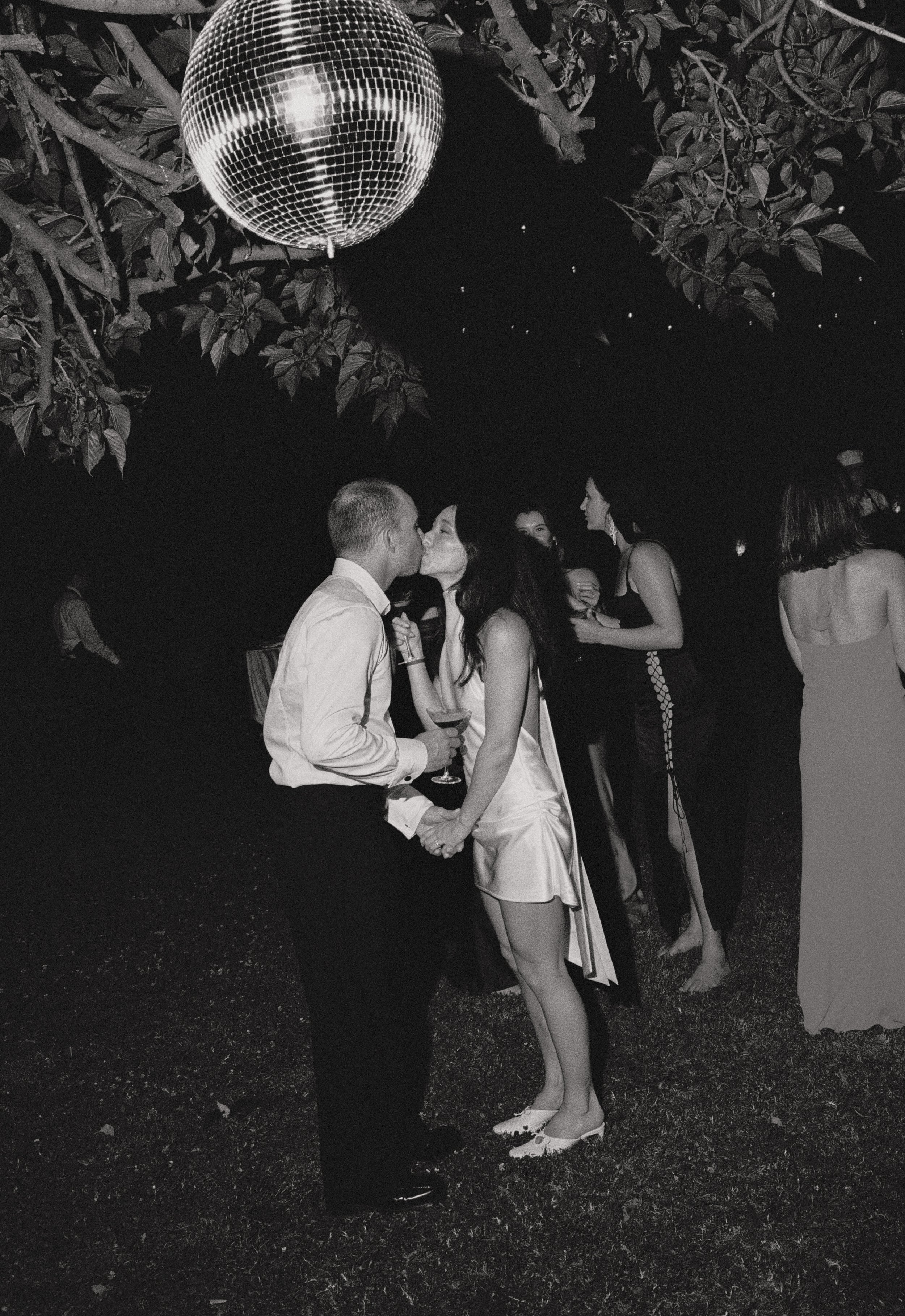 black and white image man and woman kissing under a tree and disco ball