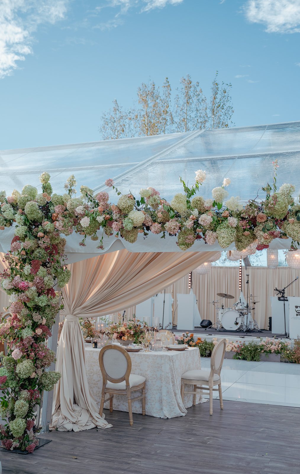 nude green and beige flowers across and down the entrance of a tent with instruments in the background and a table and chairs on the ground
