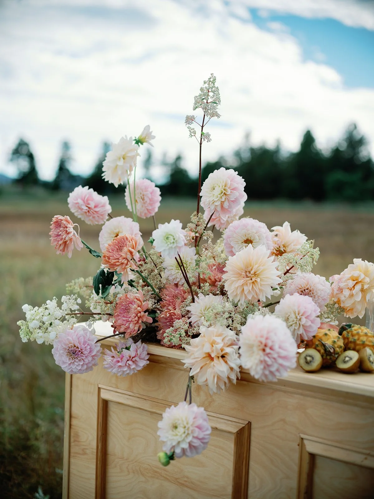 an arrangement with nude and blush flowers with kiwi fruit sitting on a wood shelf