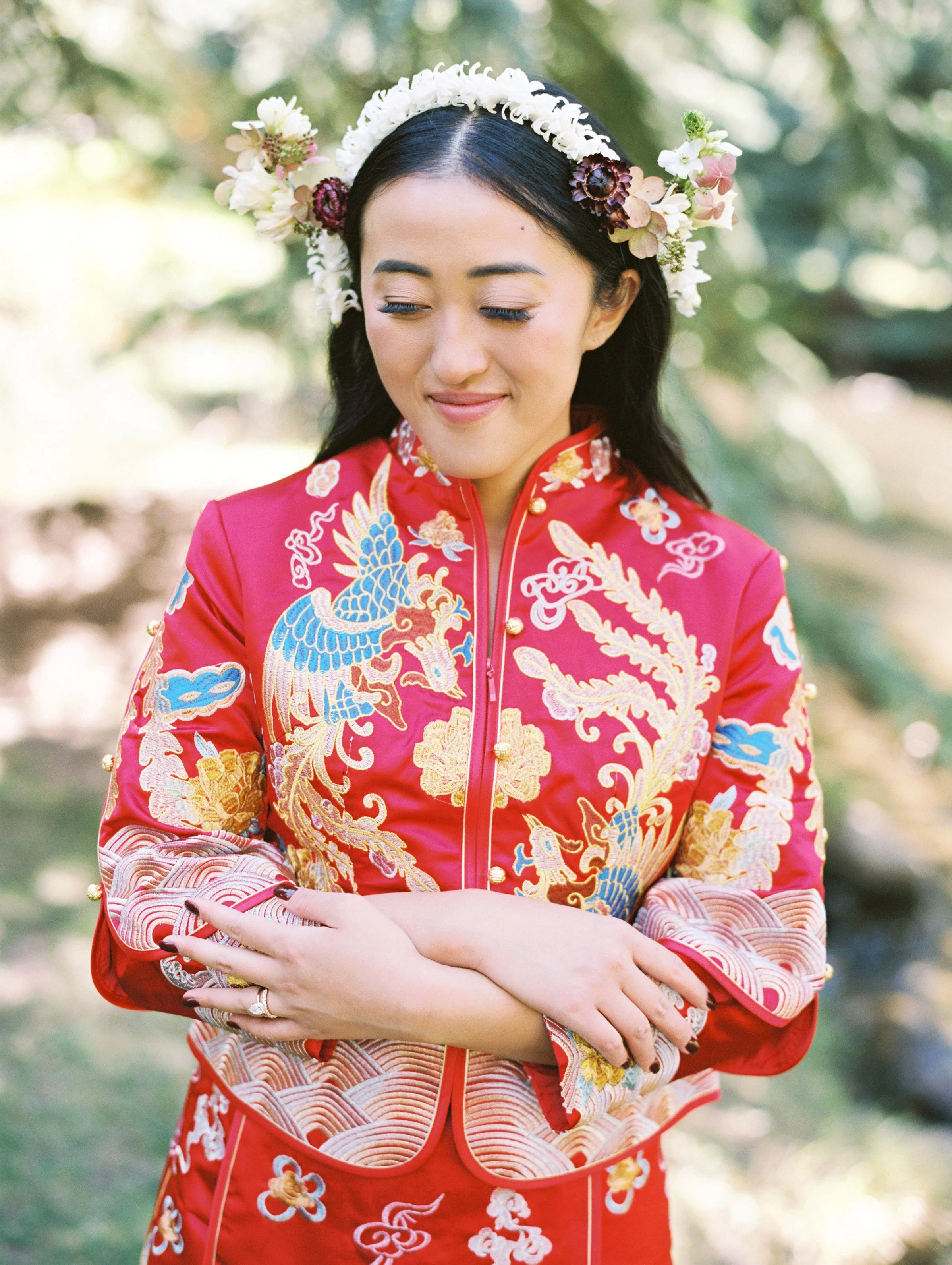 a lady in a red asian dress looking down with a white floral crown