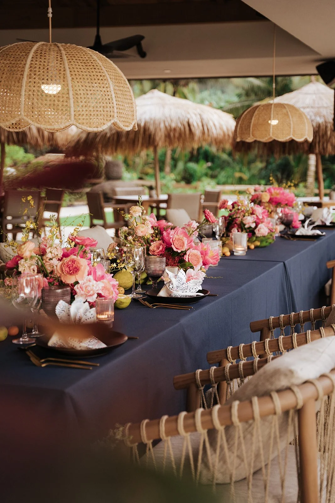 pink roses in arrangements on table with blue linen and straw canopies