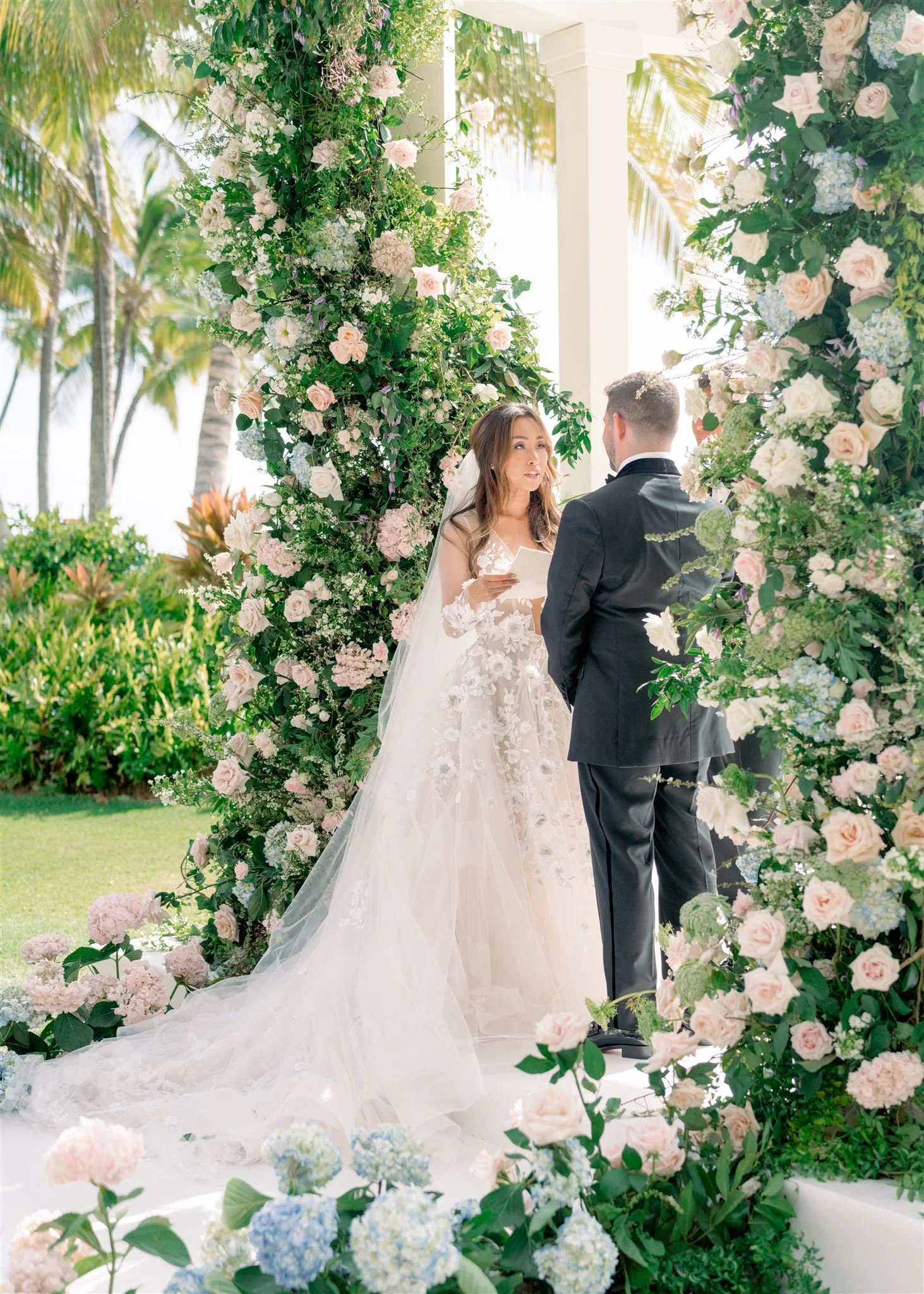 Couple under floral wedding arch exchanging vows – Hawaii Floral Design