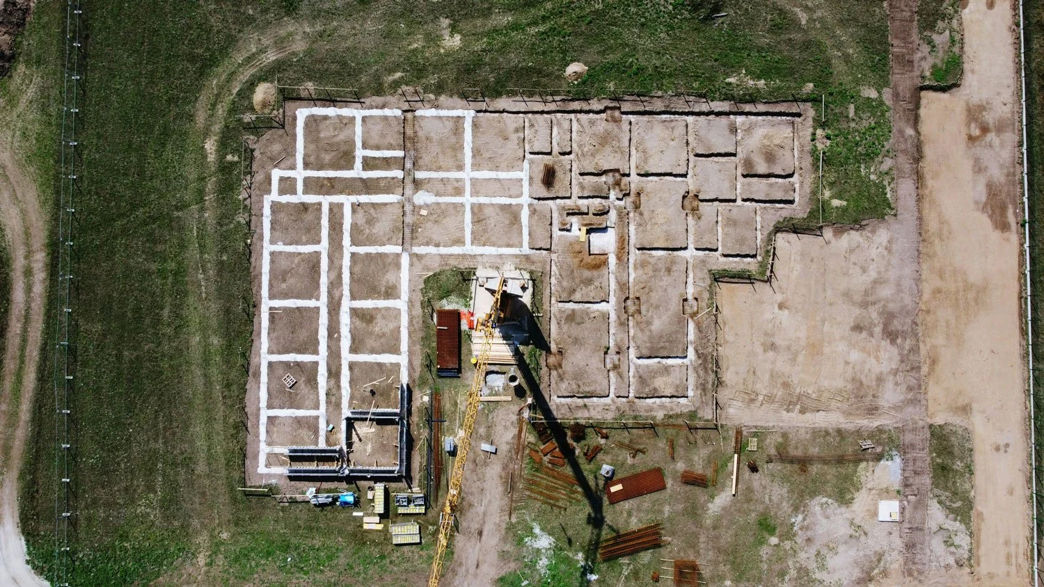 Vue aérienne d'un site de construction avec fondations en cours, une grue, et des matériaux de construction