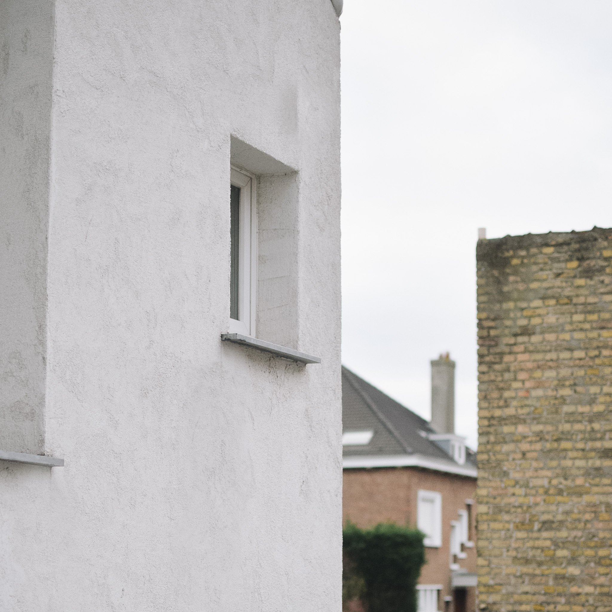 Cloison blanche avec une fenêtre, bâtiments résidentiels et ciel nuageux en arrière-plan.