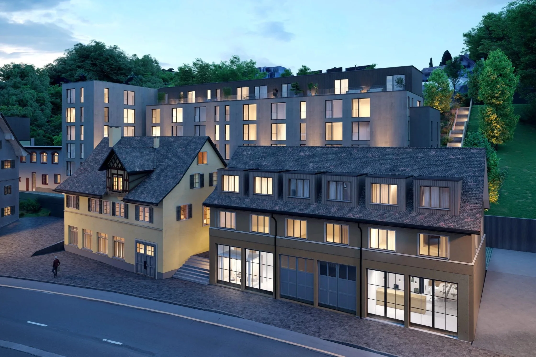 Abendansicht eines modernen Gebäudes in einer Stadt mit mehreren Etagen und großen Fenstern, umgeben von Hügeln mit Bäumen.