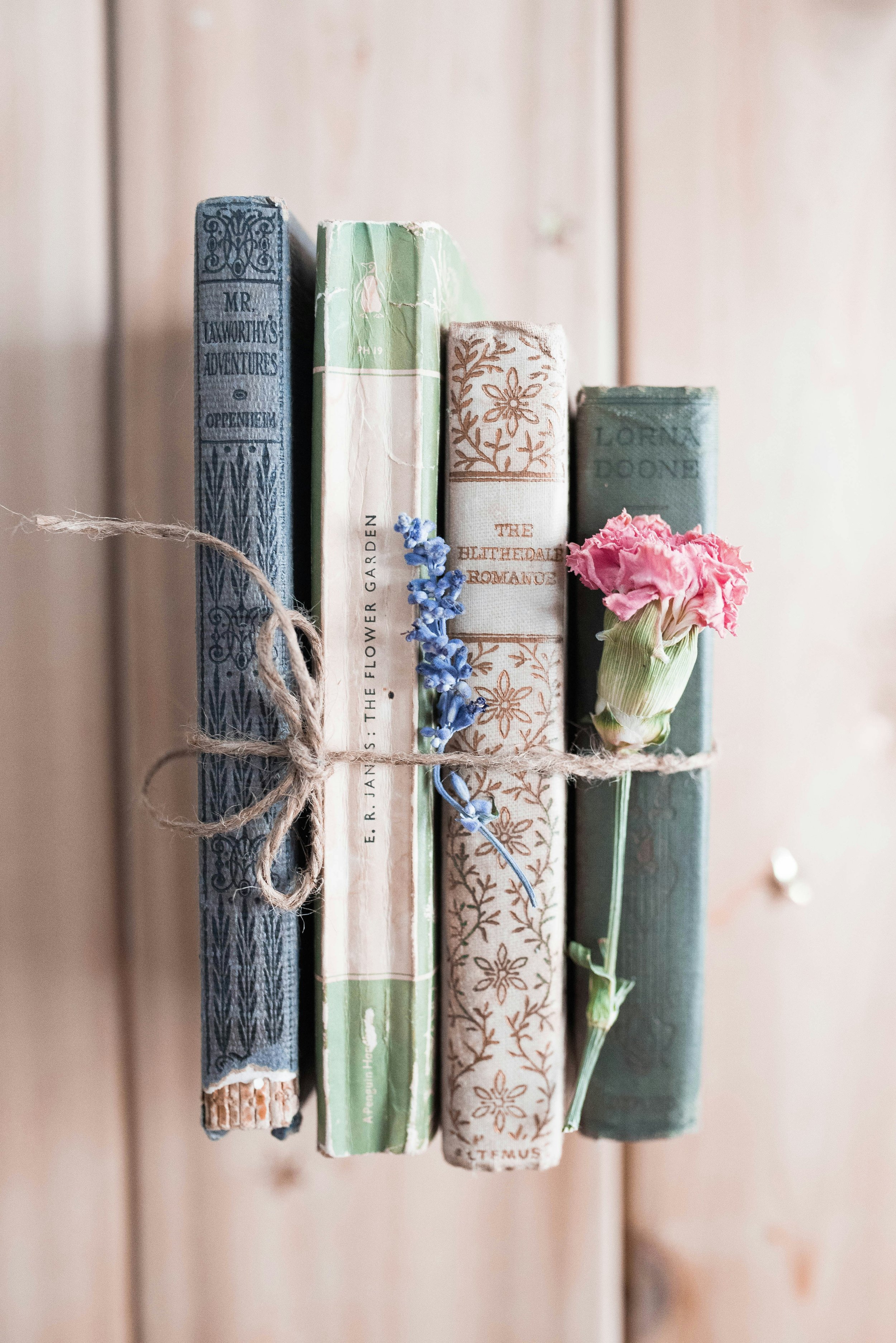 Vier alte, gebundene Bücher mit Blumen dazwischen, um eine Schnur gebunden, auf einem Holzuntergrund.