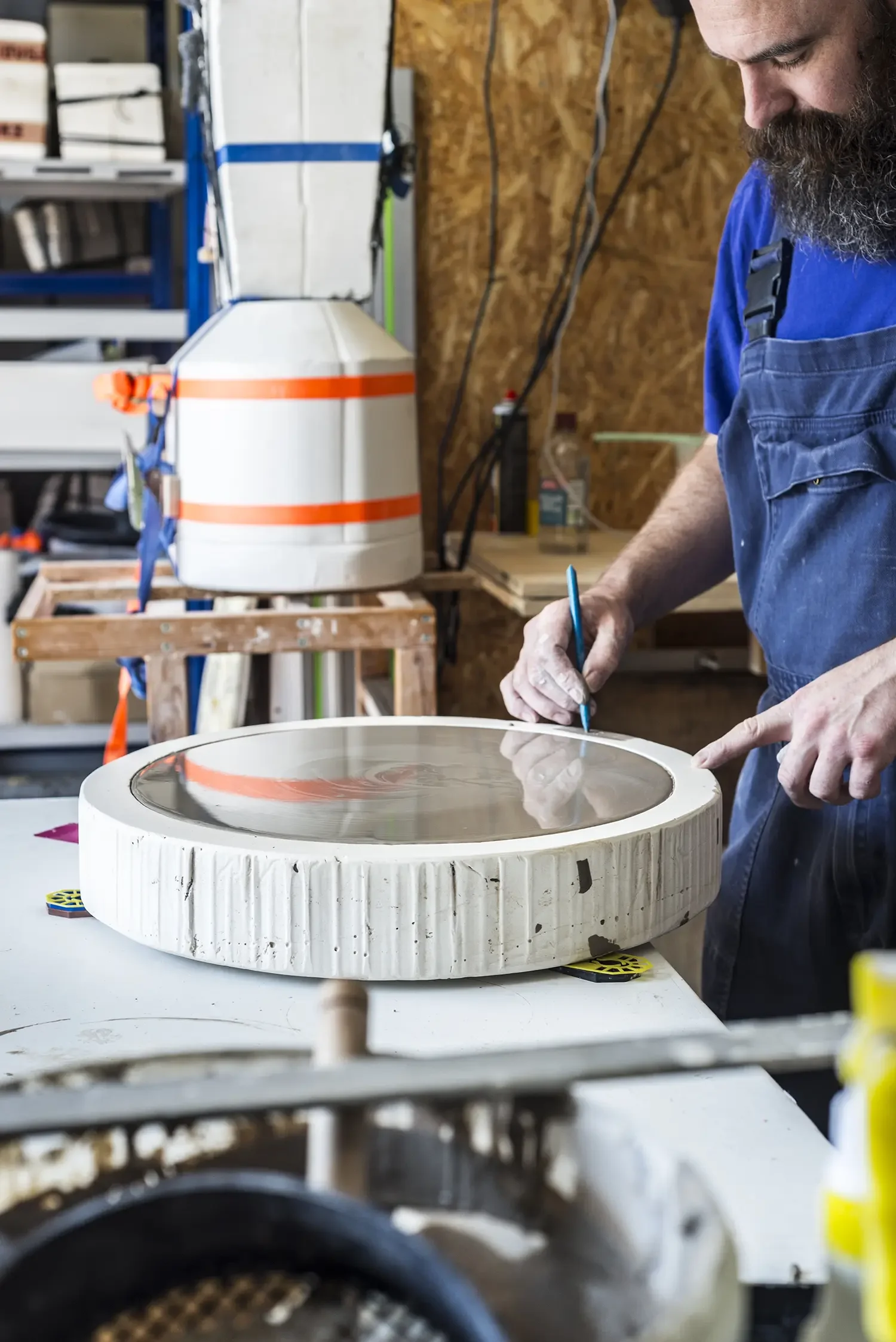 Bill Brookes who has a beard and is wearing a blue t-shirt and overalls, is working on a mould filled with liquid clay.