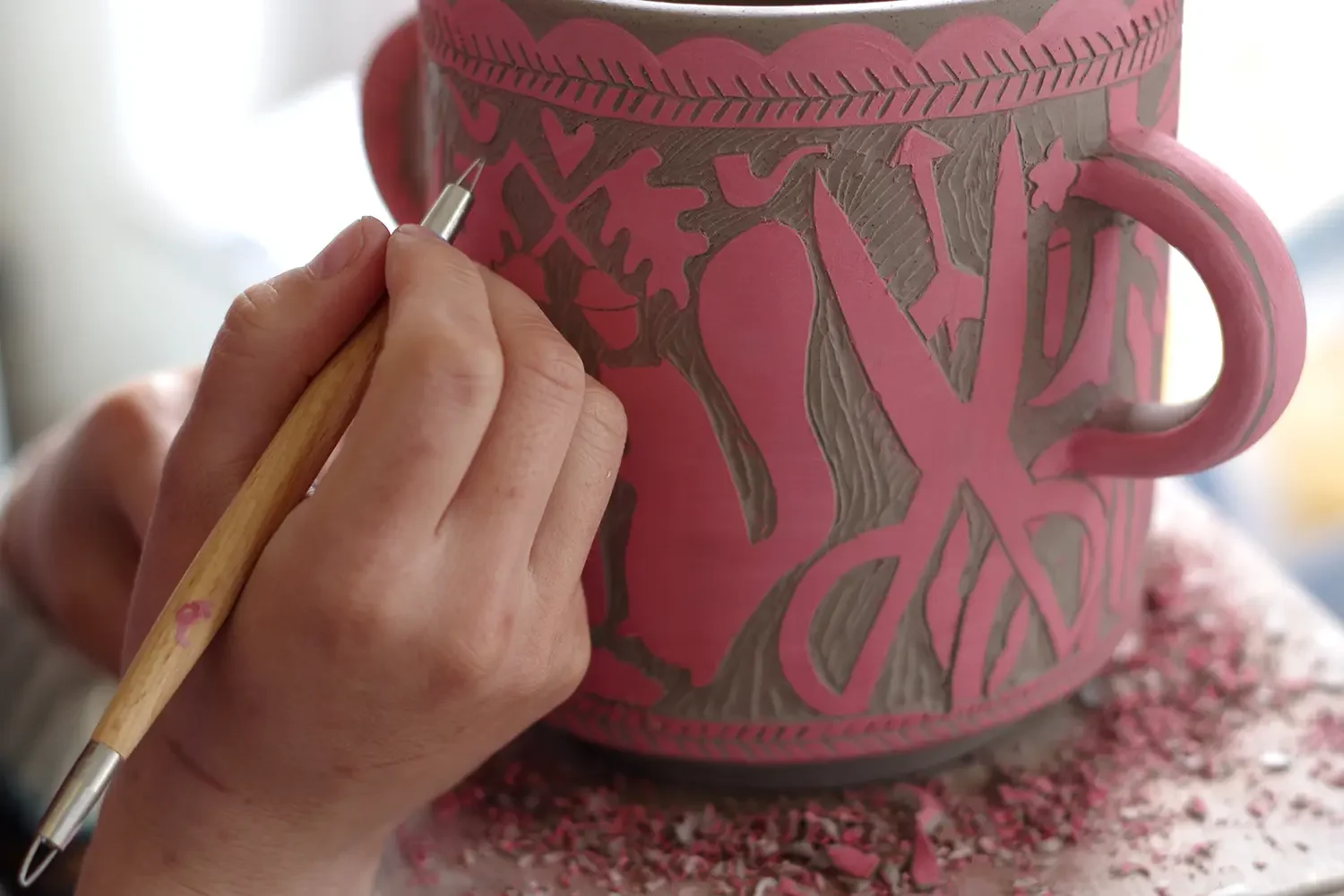 Vicky Lindo is using sgraffito to carve in a design on an amphora jug – floral and leaf designs using a fine detail tool.