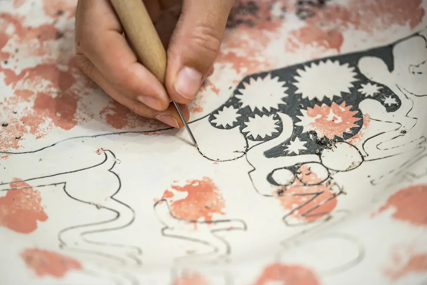 Vicky Lindo using a fine needle tool to create a detailed design in sgraffito, which includes floral and decorative elements.