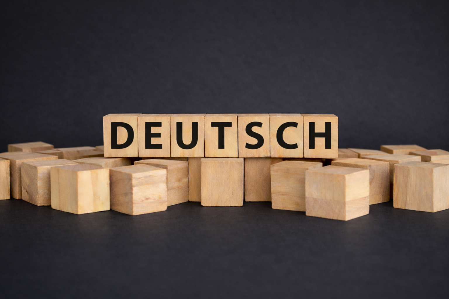 Holzbuchstaben, die das Wort 'DEUTSCH' auf dunklem Hintergrund zeigen, umgeben von weiteren Holzklötzen.