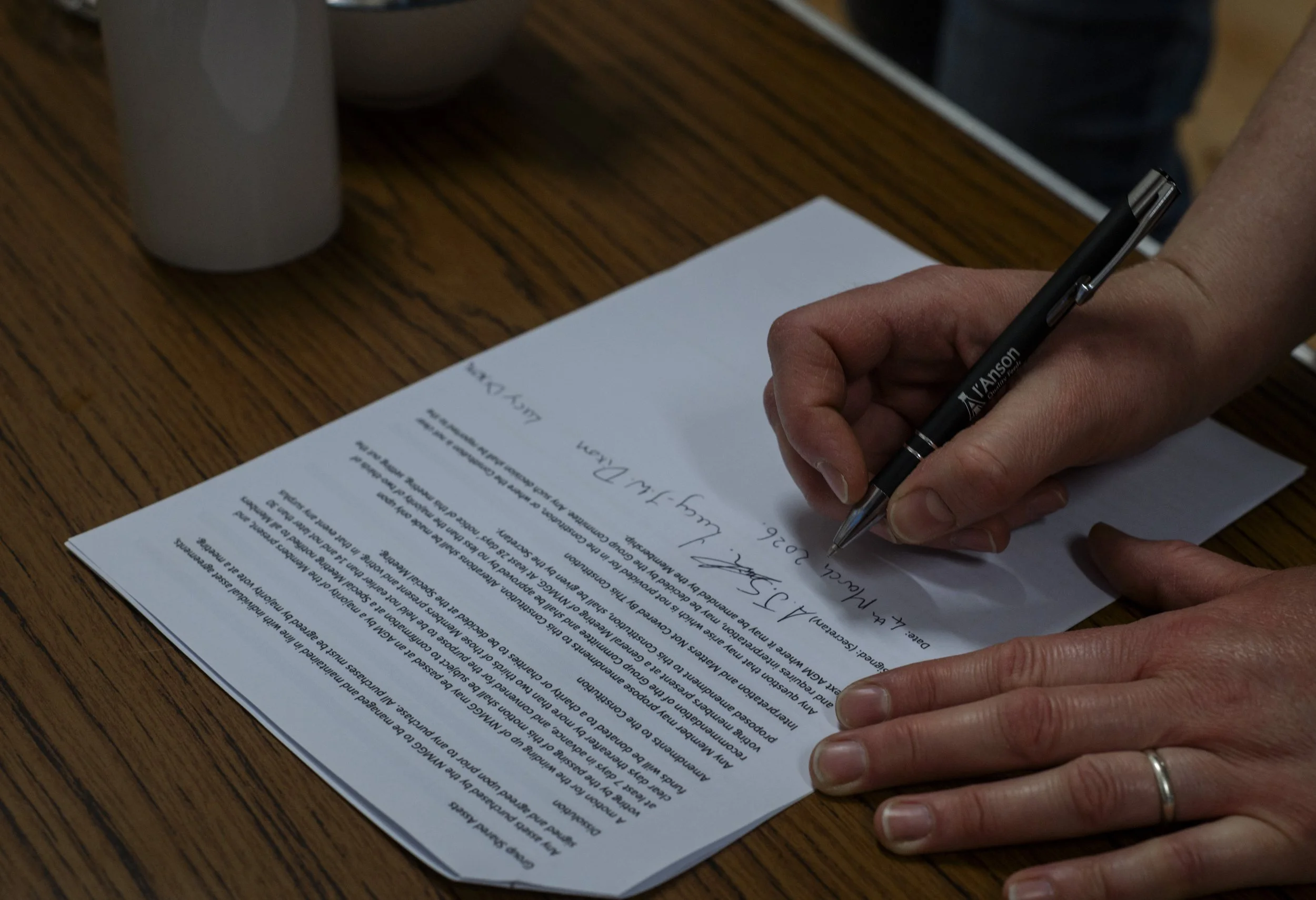 Person signing a document on a wooden table with a black pen.