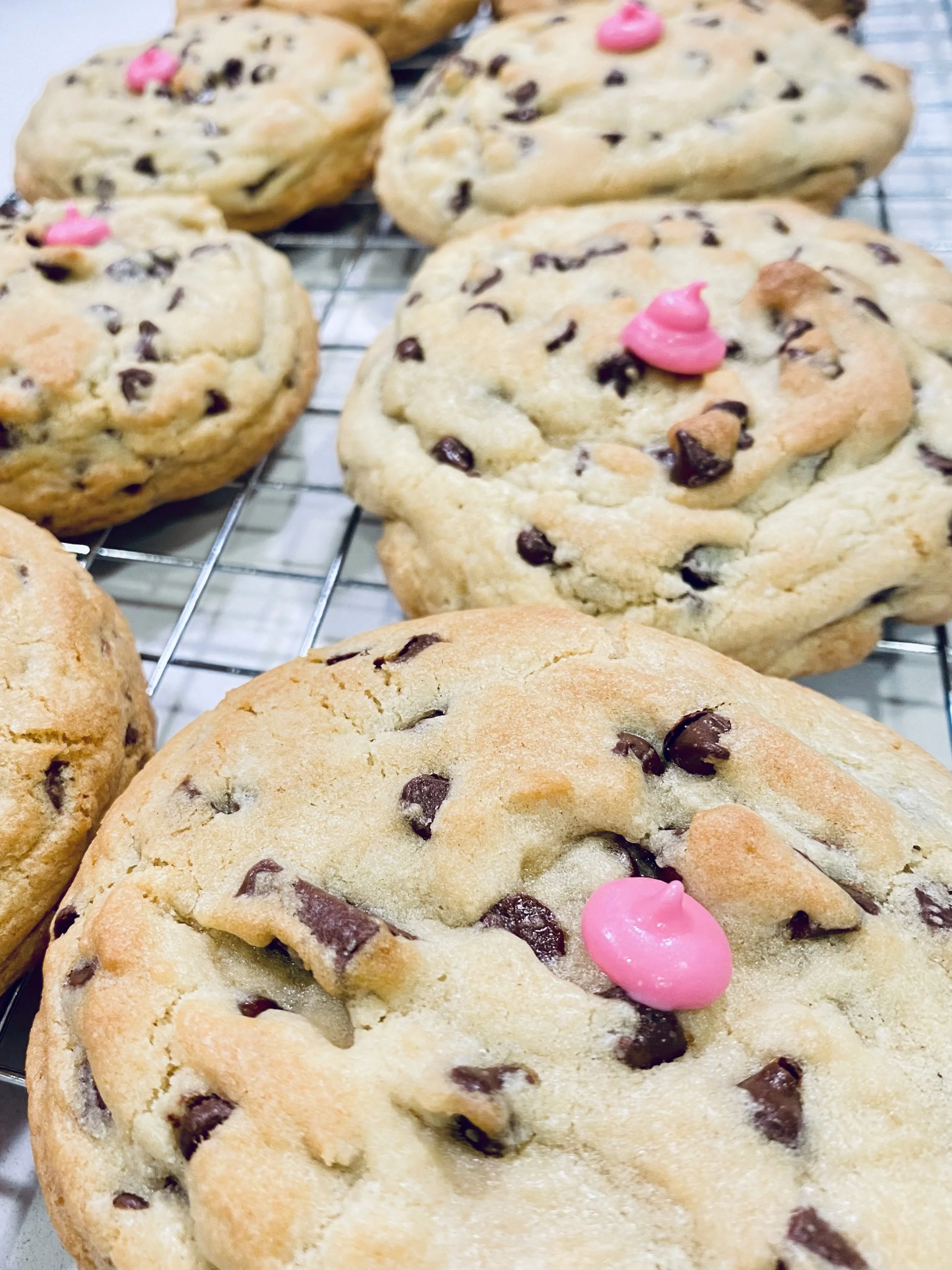 Close-up of freshly baked chocolate chip cookies with an intentionally placed PINK CHIP cooling on a wire rack.