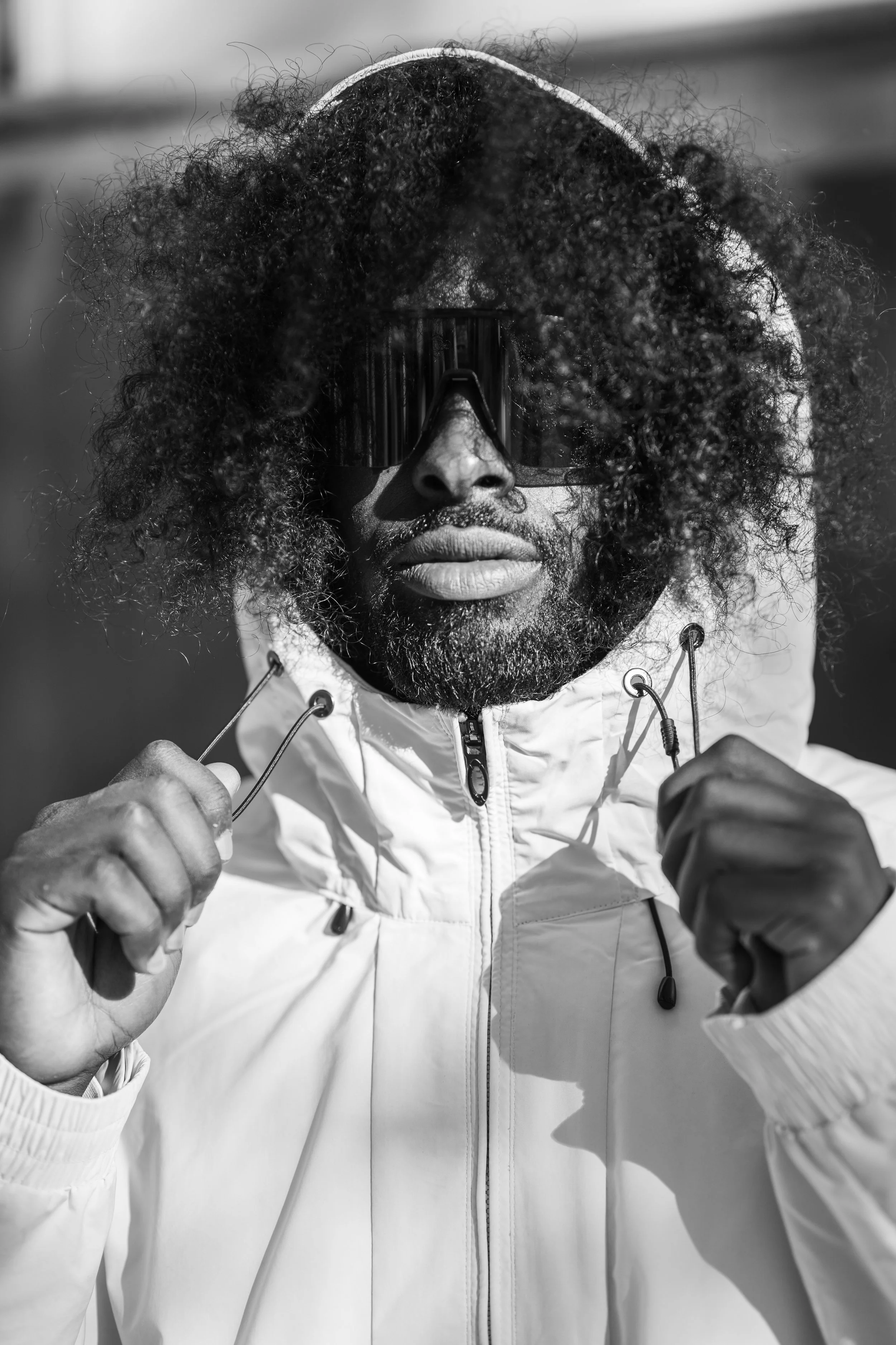 Striking black and white portrait of a man in a hooded jacket and sunglasses, showcasing modern street style, confidence, and bold urban fashion.