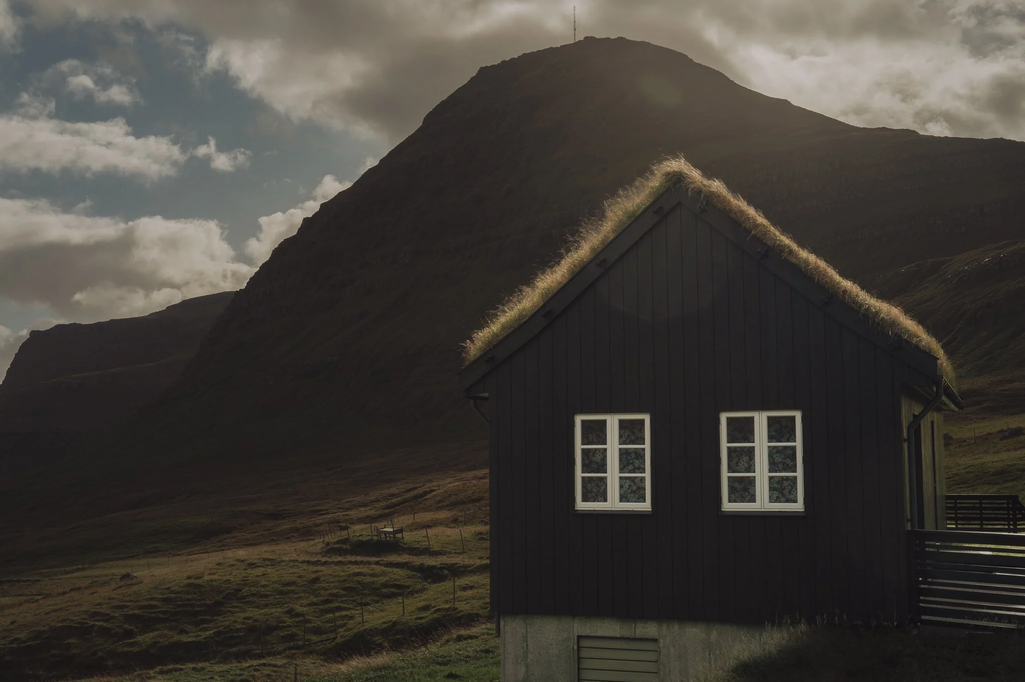 A house with a grass-covered roof situated near mountain terrain under cloudy sky.