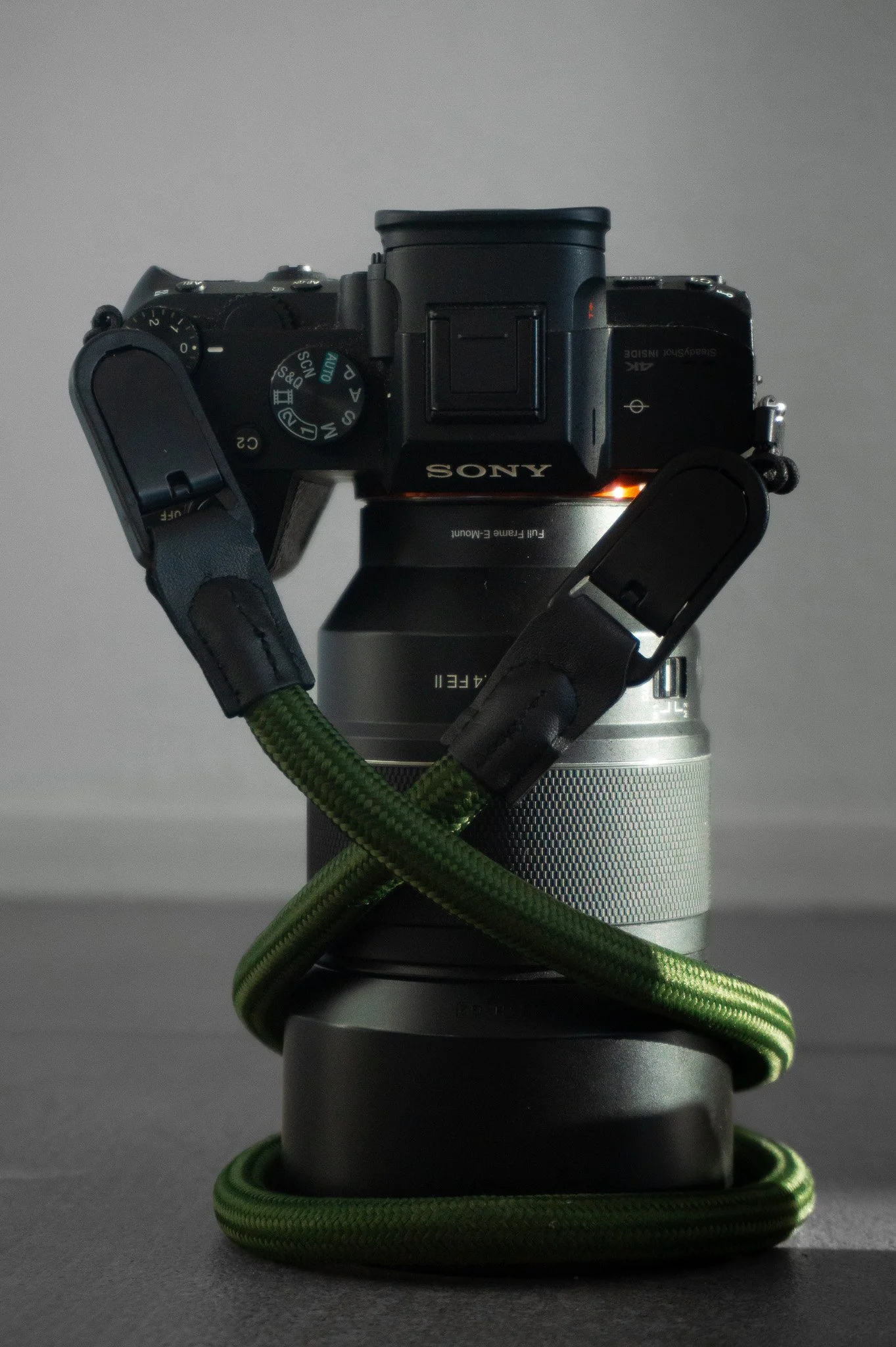 A Sony camera mounted on a camera lens, with a green and black striped strap wrapped around the lens and base.