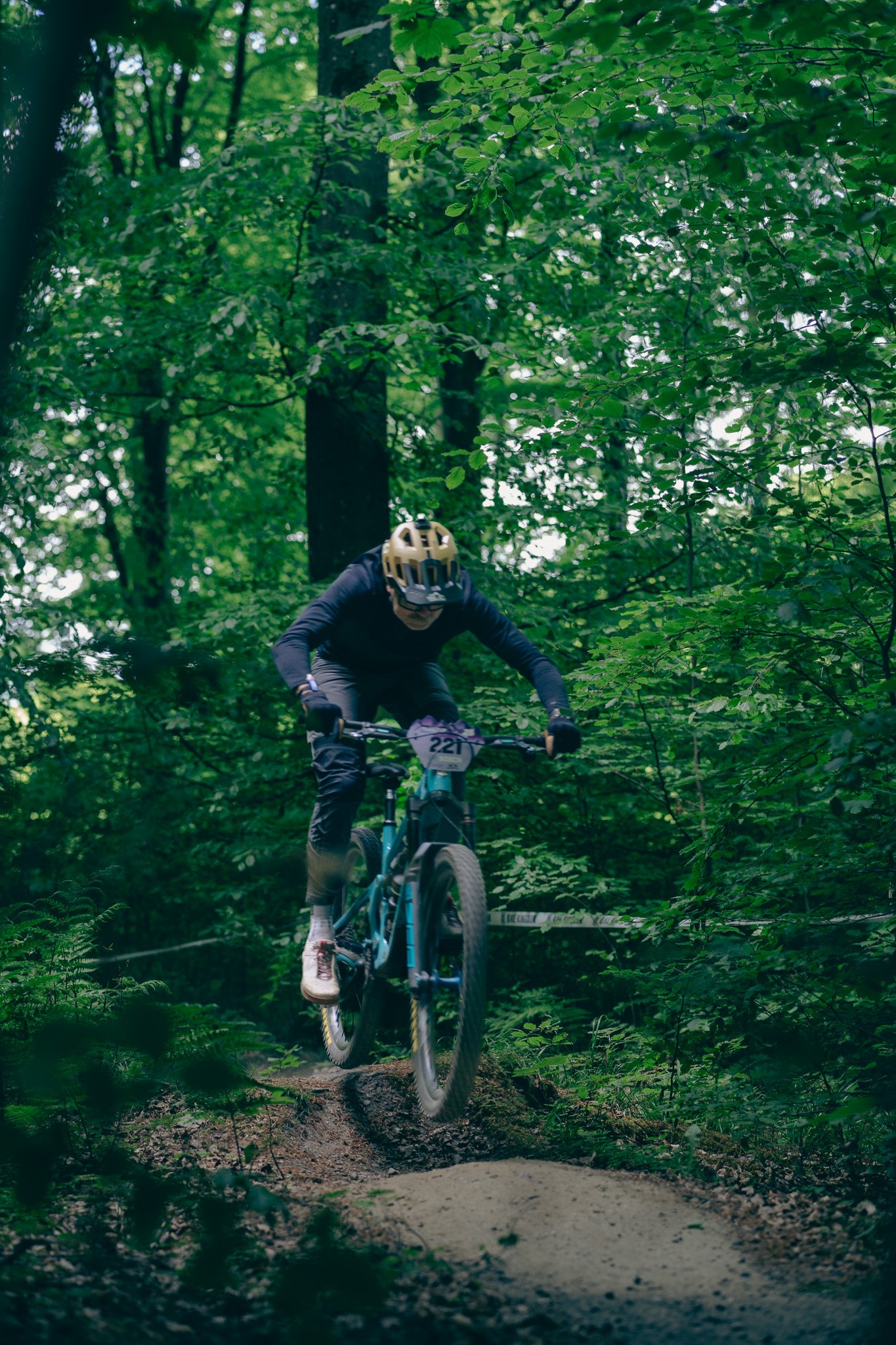 A person wearing a helmet and dark clothing riding a mountain bike on a wooded trail.