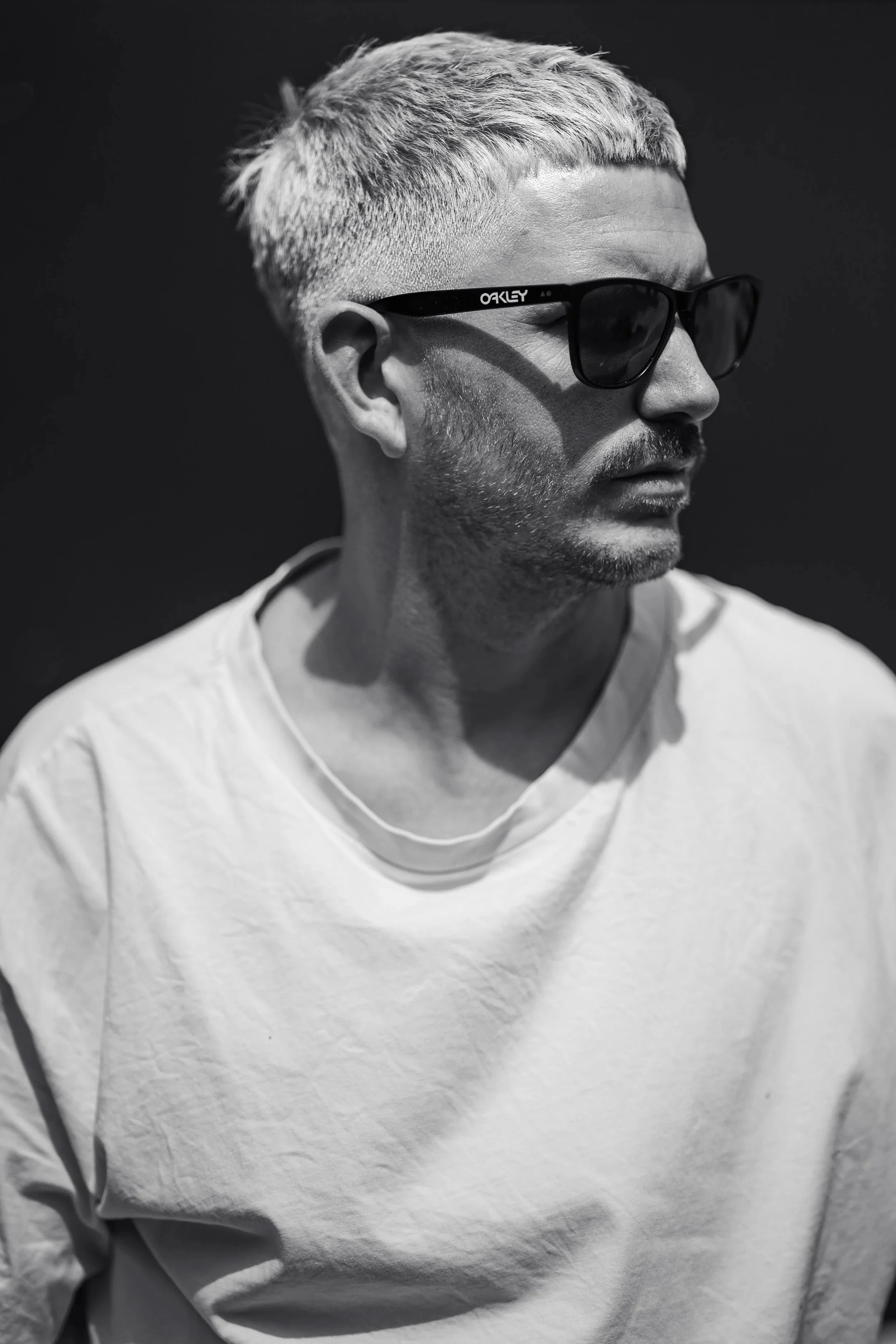 A minimalist black-and-white portrait of a man wearing sunglasses, captured in natural light with strong contrast and a clean, modern composition.