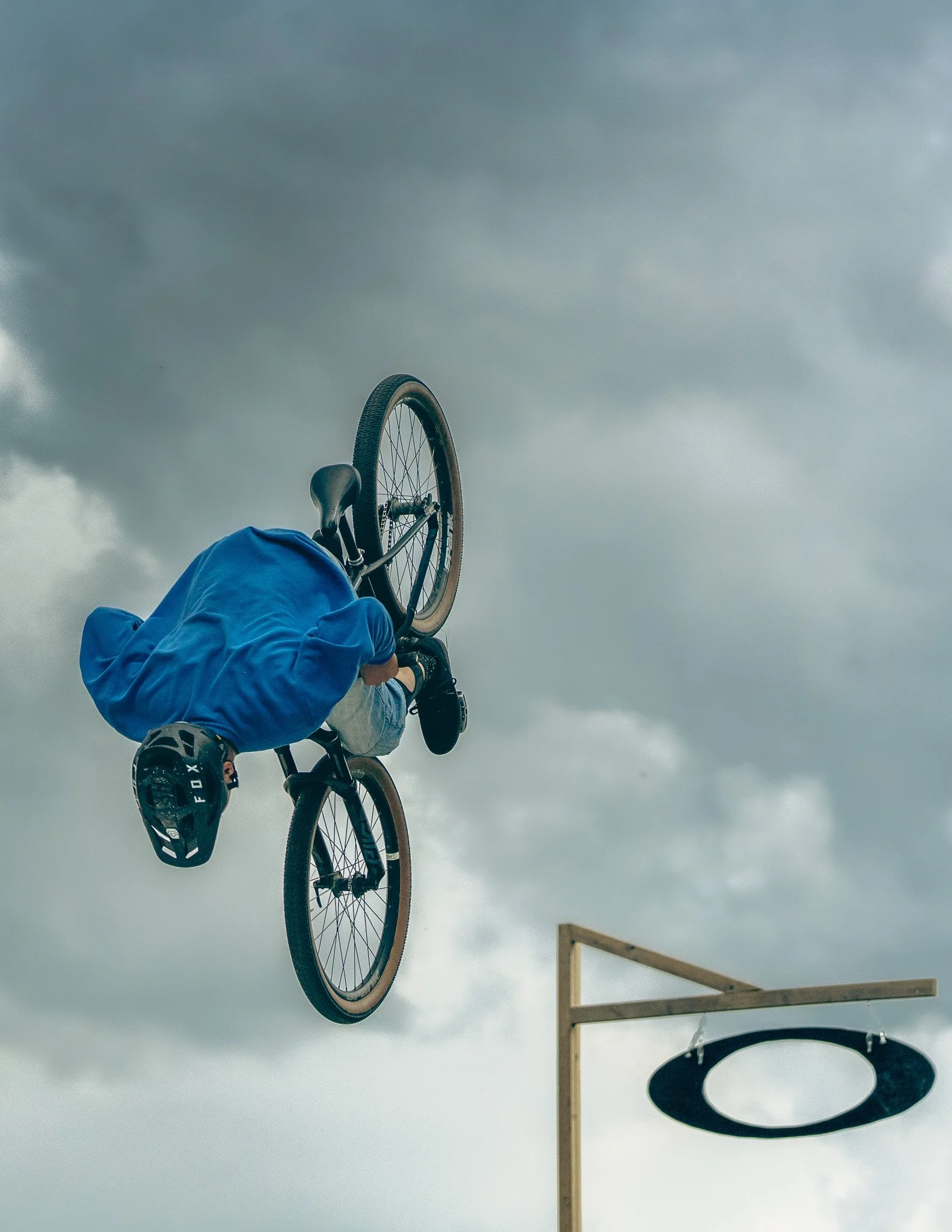 Person in blue jacket and helmet performing a BMX stunt on a dirt ramp during cloudy weather