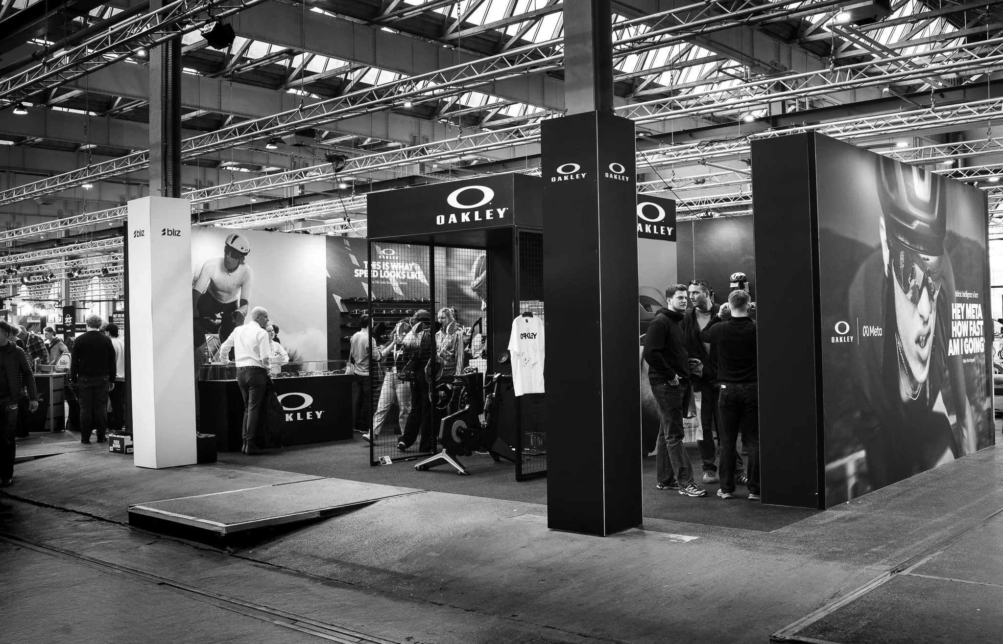 An indoor event showcasing Oakley sports eyewear, with a booth displaying sunglasses and promotional materials, and people engaging with staff and products.