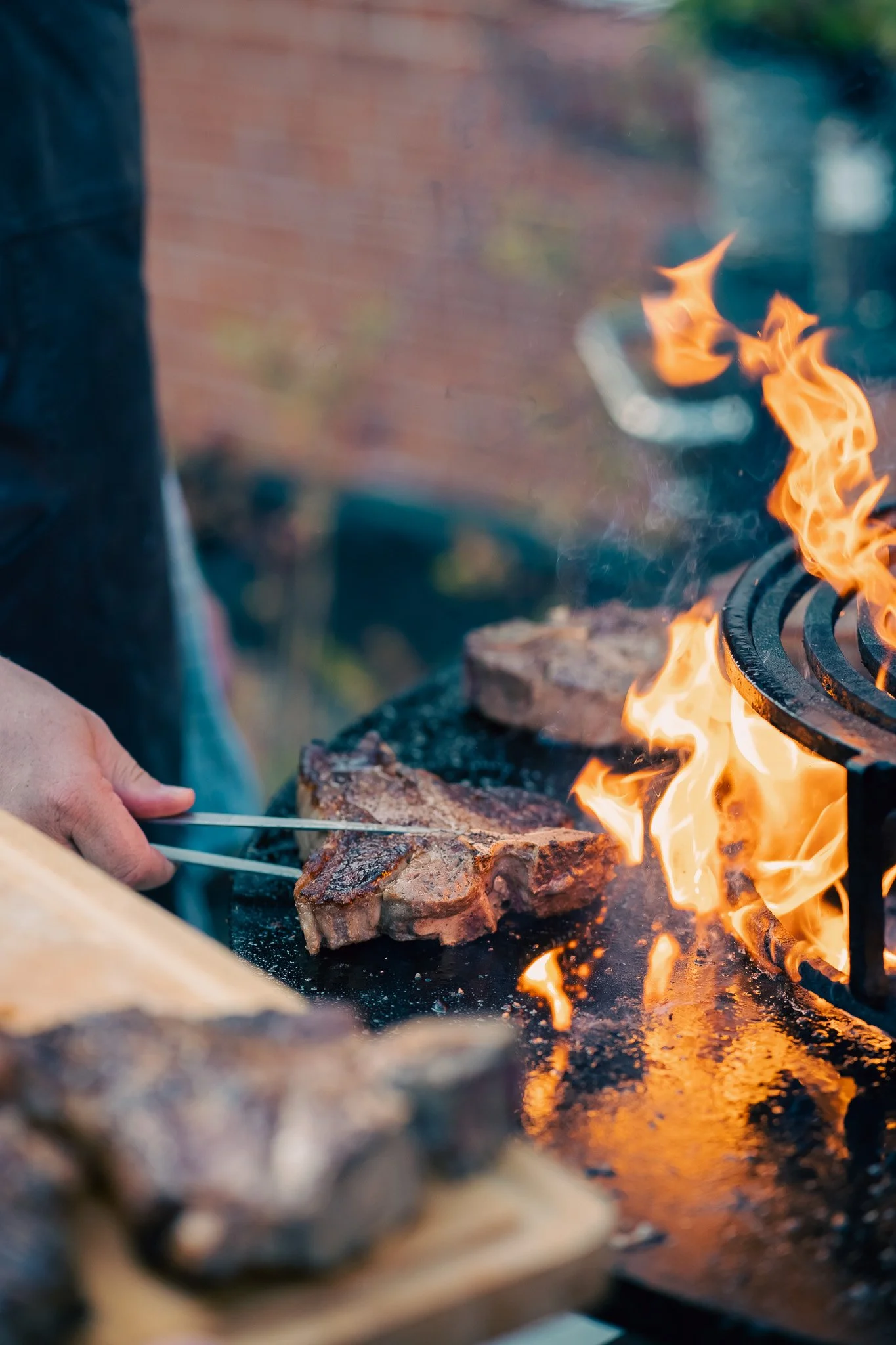 Someone grilling steaks over an open flame on a barbecue grill.