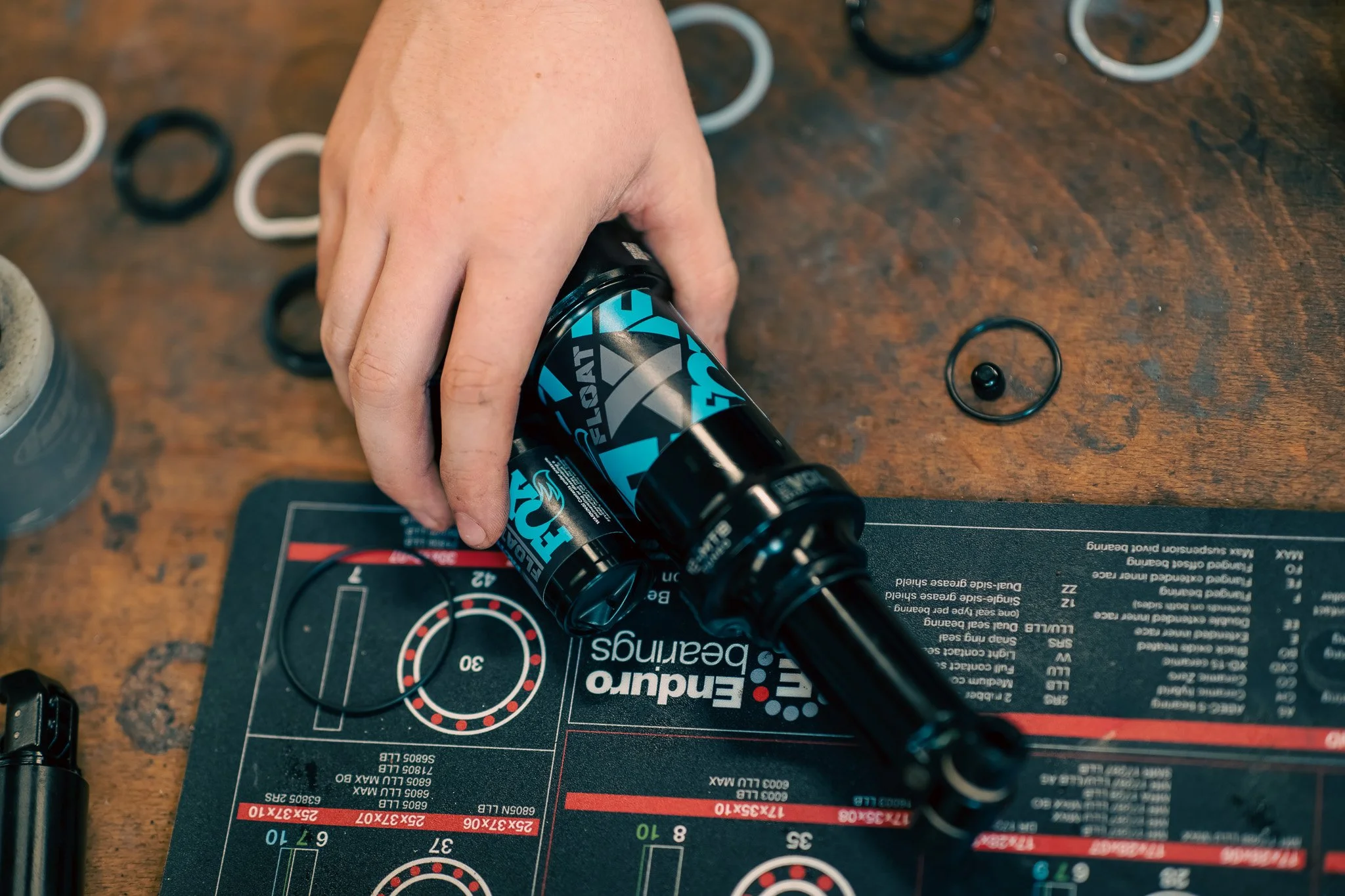 Person's hand handling a black and blue energy gel shot bottle over a hockey training mat, with black and white rubber bands scattered around on a wooden surface.