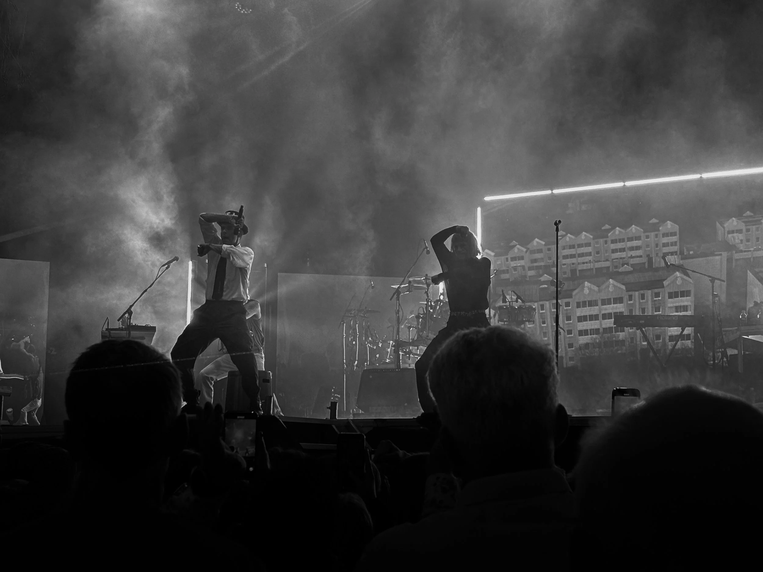 Black and white concert photograph capturing live performers on stage amid dramatic lighting and smoke, conveying energy, atmosphere, and the intensity of a live music experience.