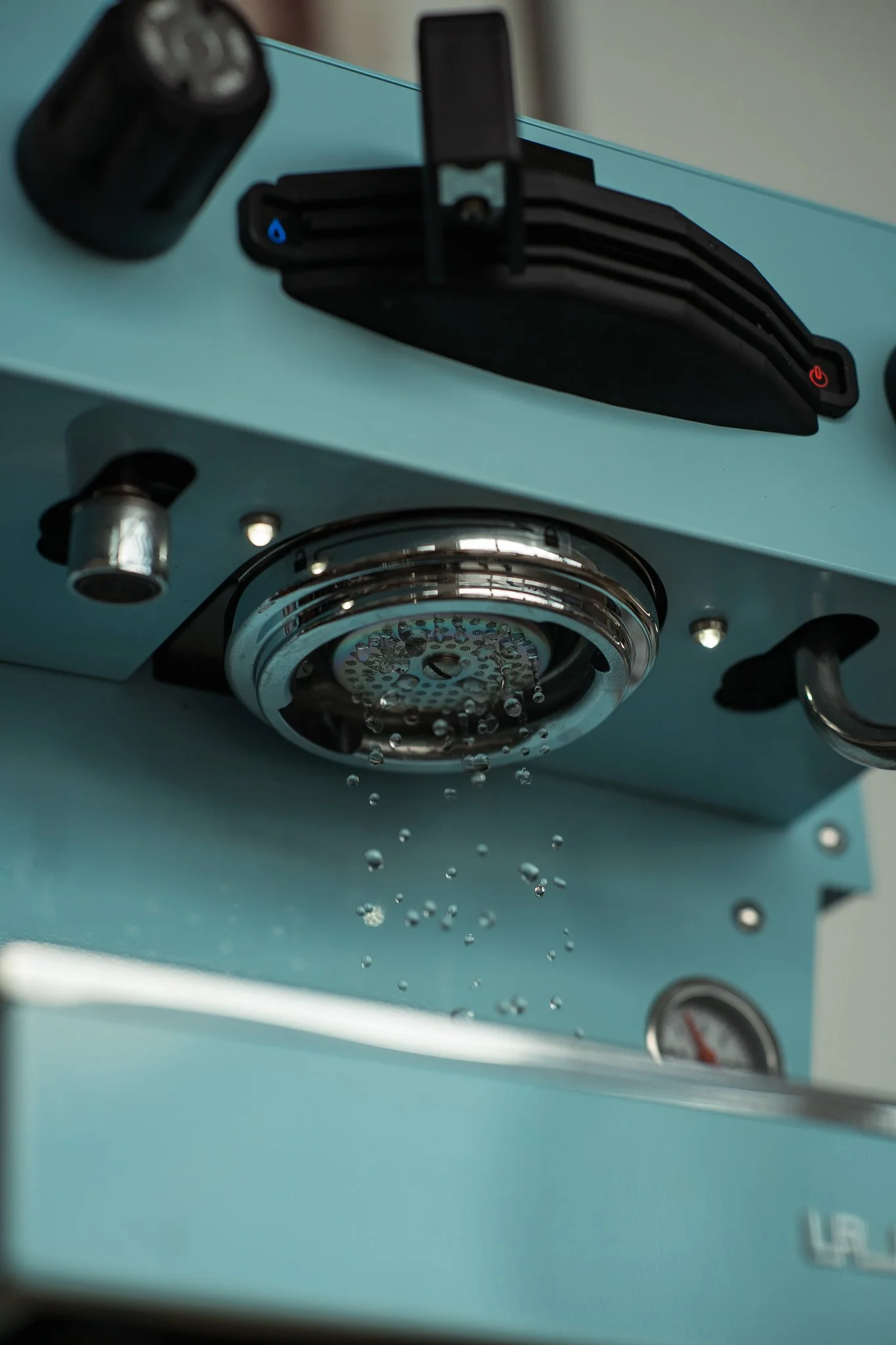 Close-up of a teal-colored coffee machine with water dripping from the spout.
