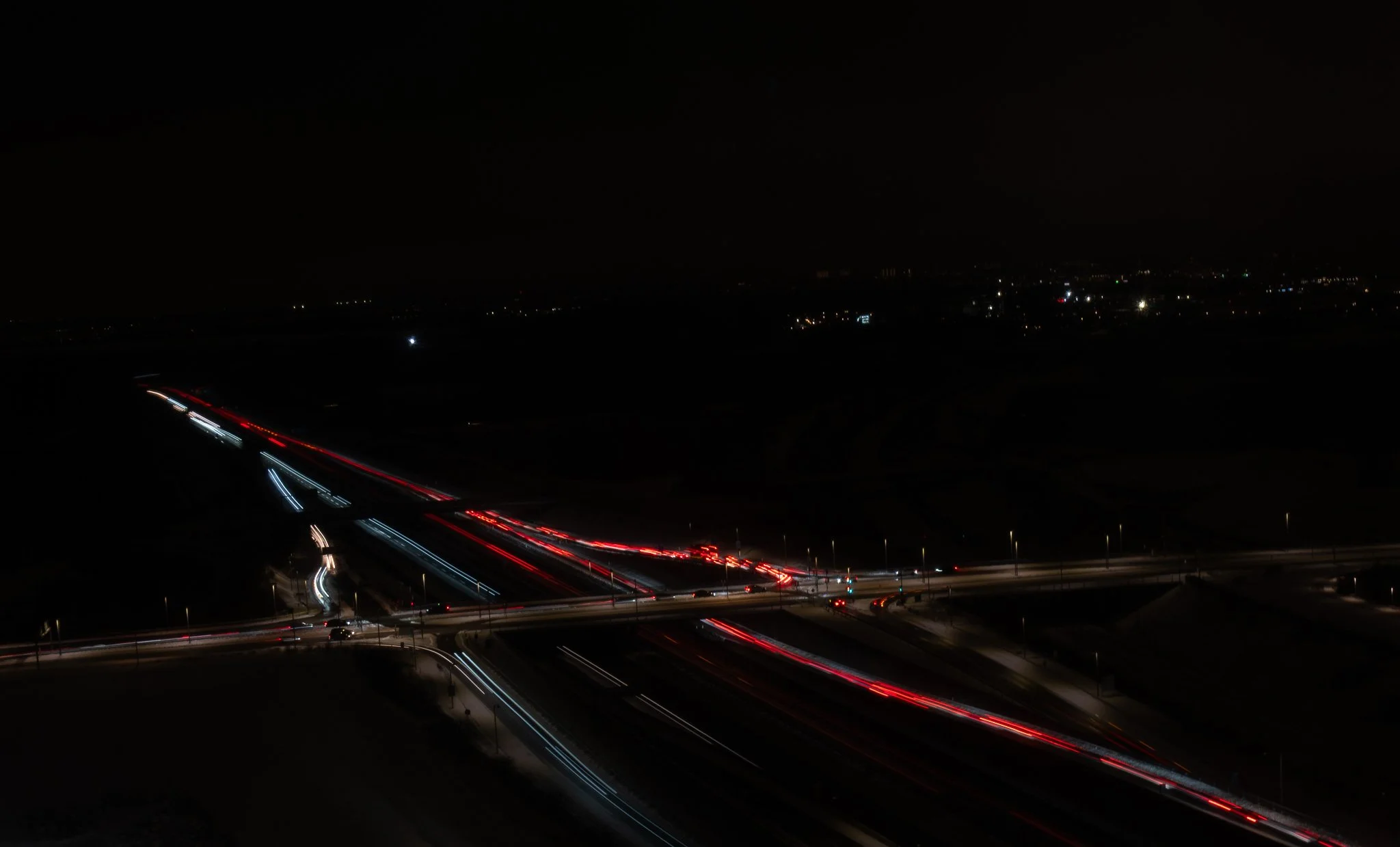 Nighttime aerial view of a busy highway with streaks of red and white lights from moving vehicles, under a dark sky with distant city lights.