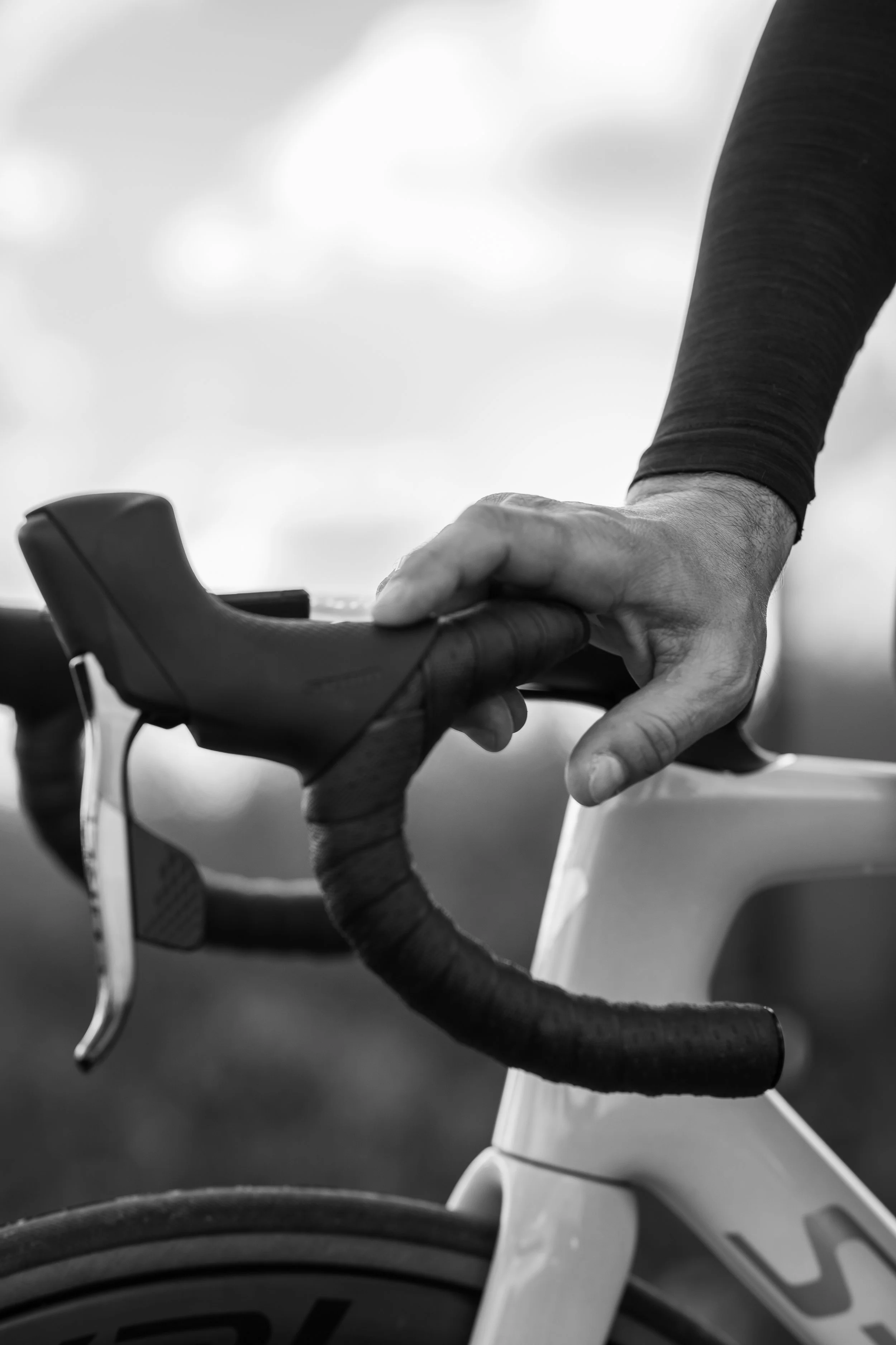 Close-up of a person gripping the handlebars of a road bicycle, with a focus on the hand and handlebar.