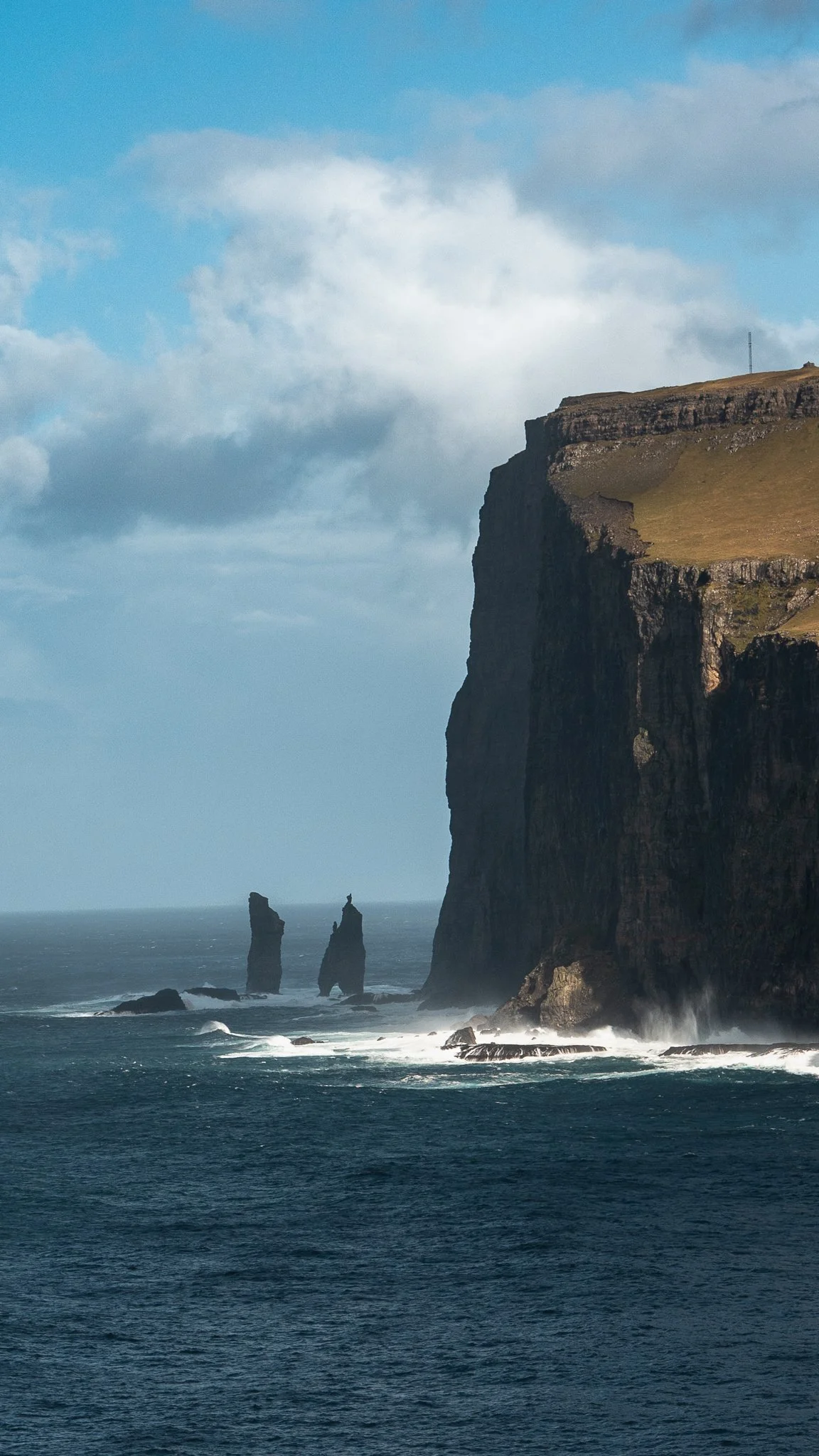 Cliffs and sea stacks along a rugged coastline under a partly cloudy sky.