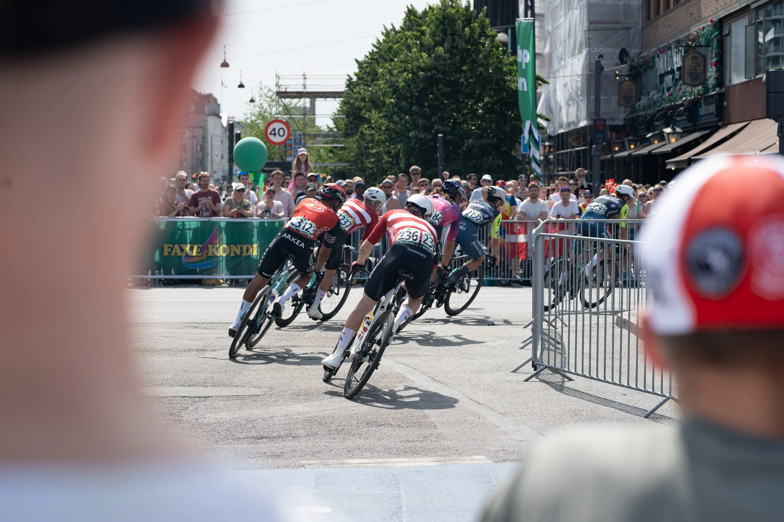 High-speed criterium cycling race in an urban setting, with riders cornering sharply as crowds line the streets, capturing intensity, competition, and city race atmosphere.