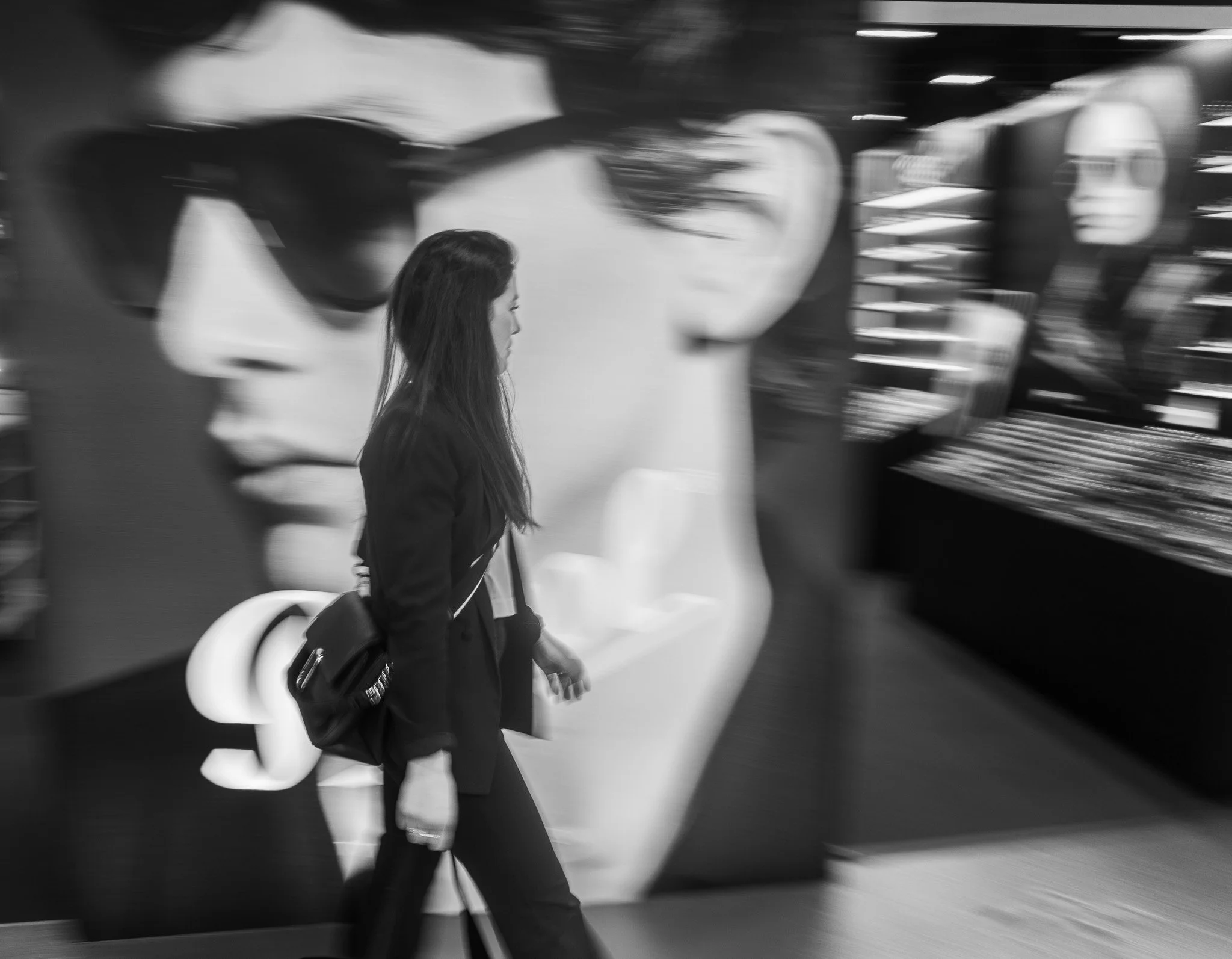 A woman walking past a large black and white advertisement of two women wearing sunglasses in an indoor shopping area.
