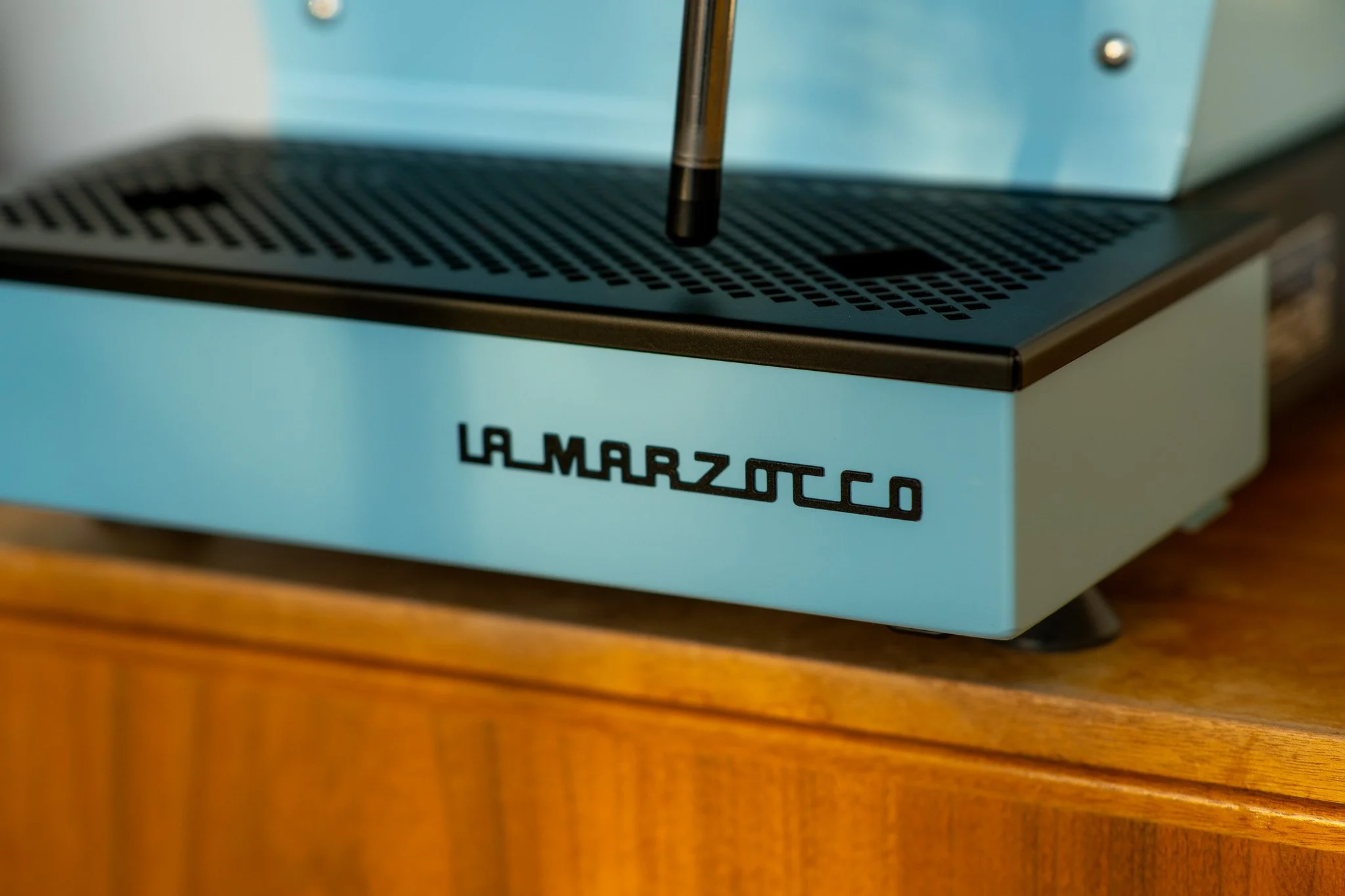 Close-up of a vintage La Marzocco espresso machine with a light blue body, placed on a wooden surface.