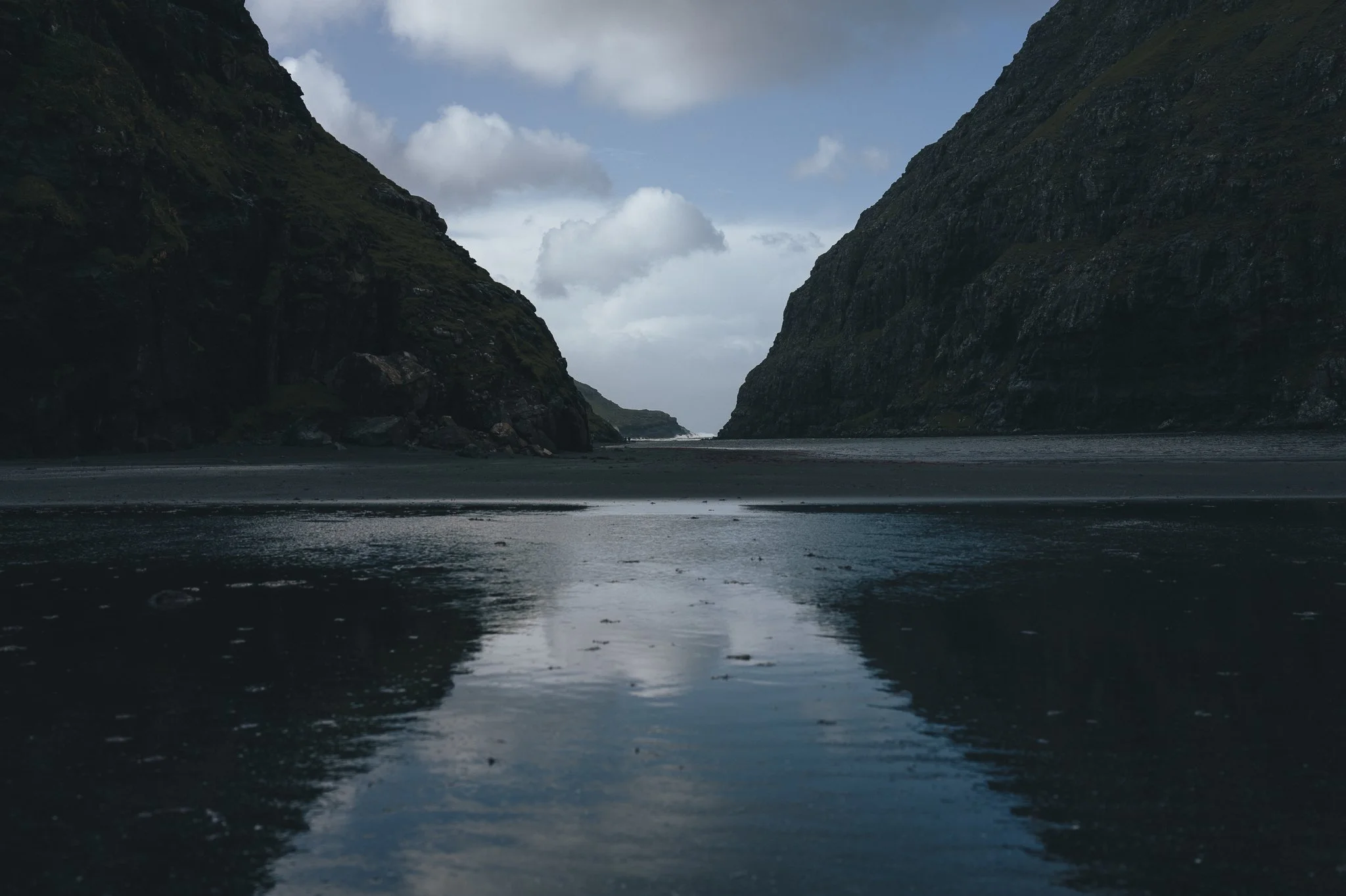 A narrow fjord with steep, green-covered cliffs on either side under a cloudy sky.