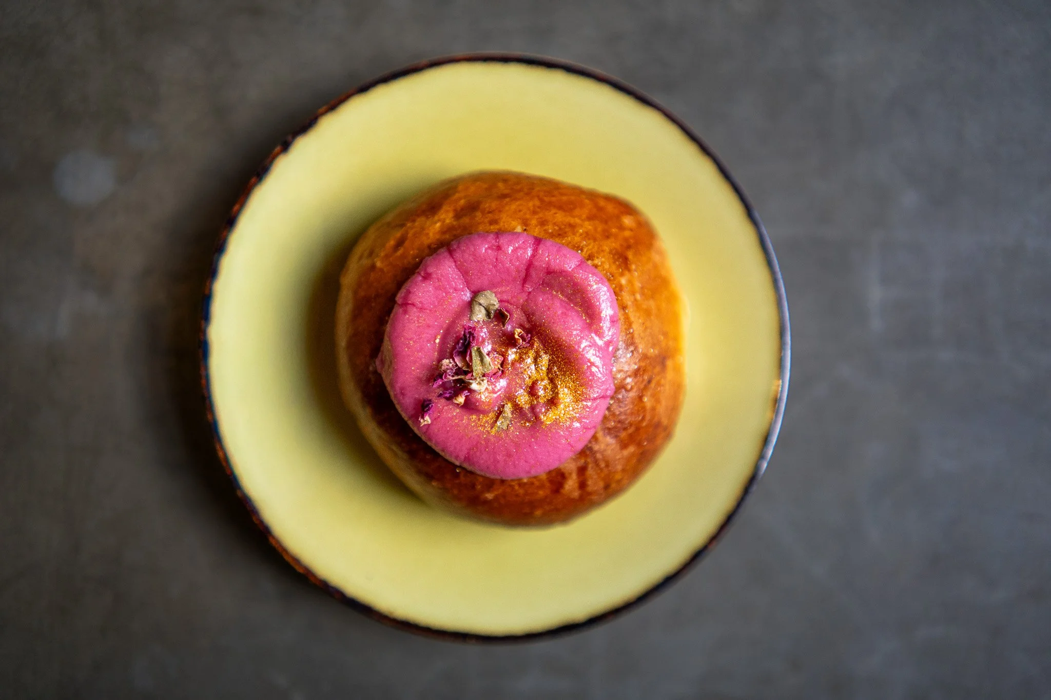 A sliced mango with a scoop of pink sorbet and rose petals on top, served on a black plate.