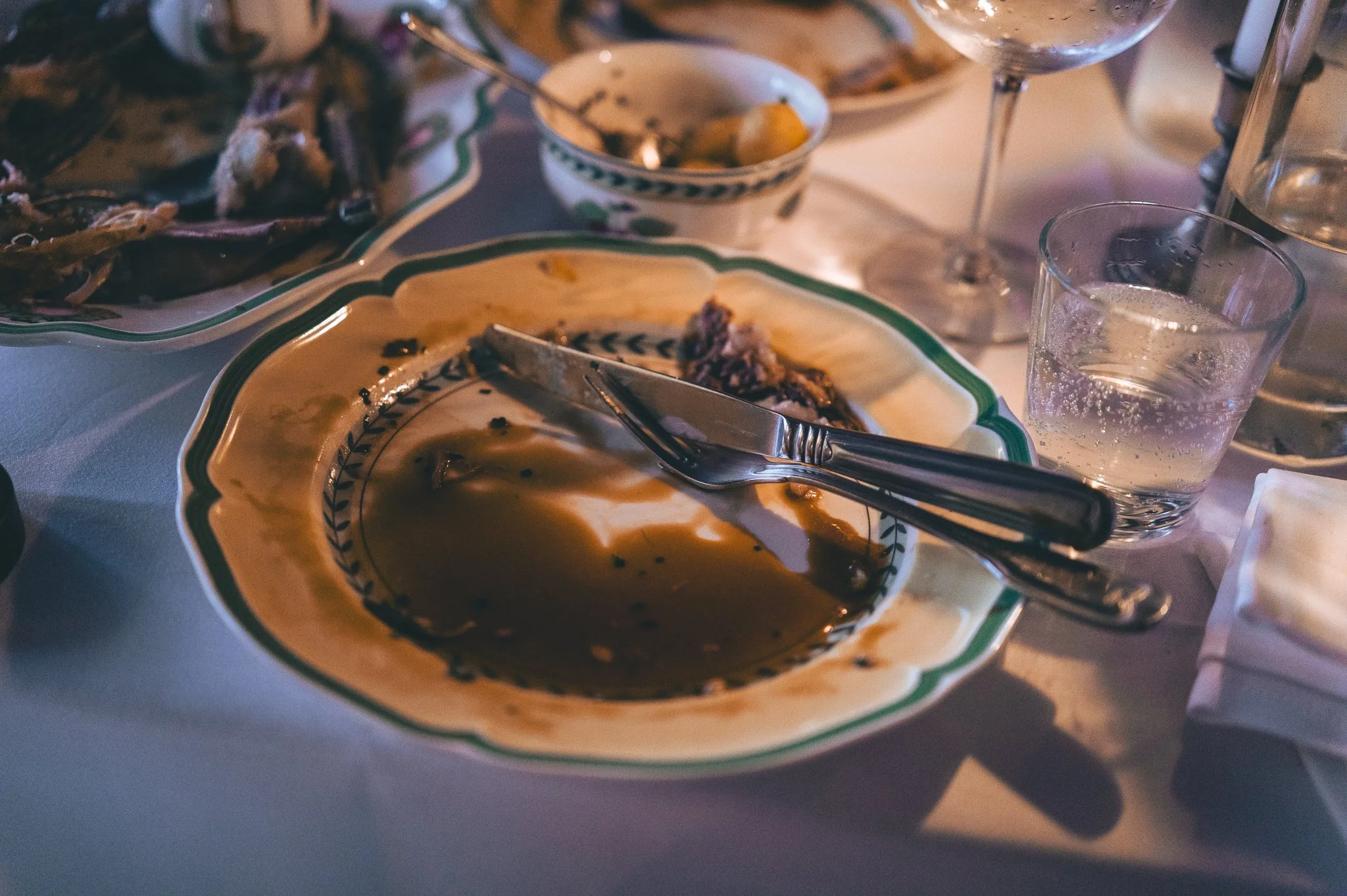 Empty dishes and glasses on a dining table after a meal. Some dishes have leftover food, and there are drinking glasses, some with ice and water.