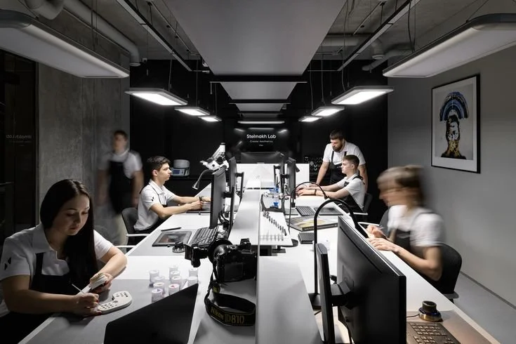 People working at desks with computers in a modern, dark-themed office or lab environment.