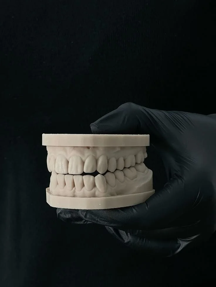 A hand wearing a black glove holding a dental mold of teeth against a black background.