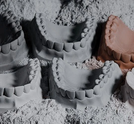 Dental molds of teeth in different colors on sandy surface.