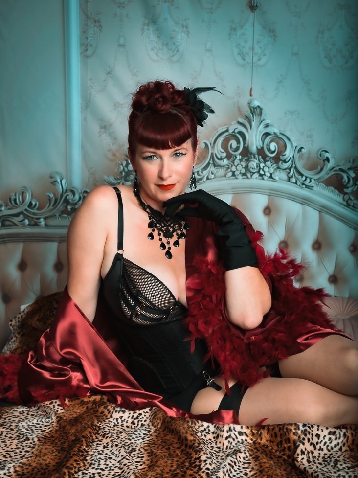 Femme portant une robe et des accessoires noirs et rouges, assise sur un lit avec une tête de lit décorative et une couverture en léopard.